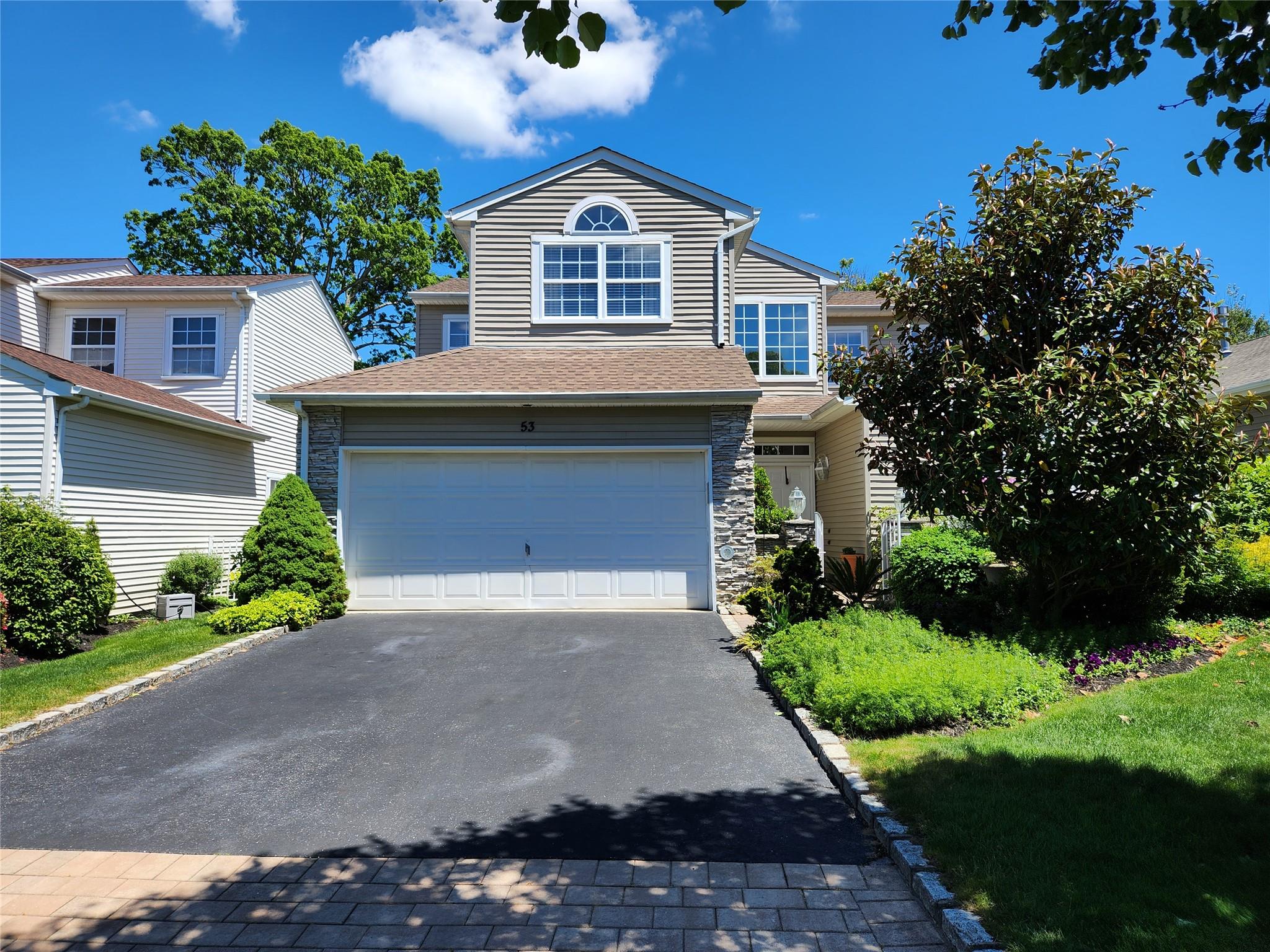 View of front facade with driveway, a garage, a shingled roof, and stone siding