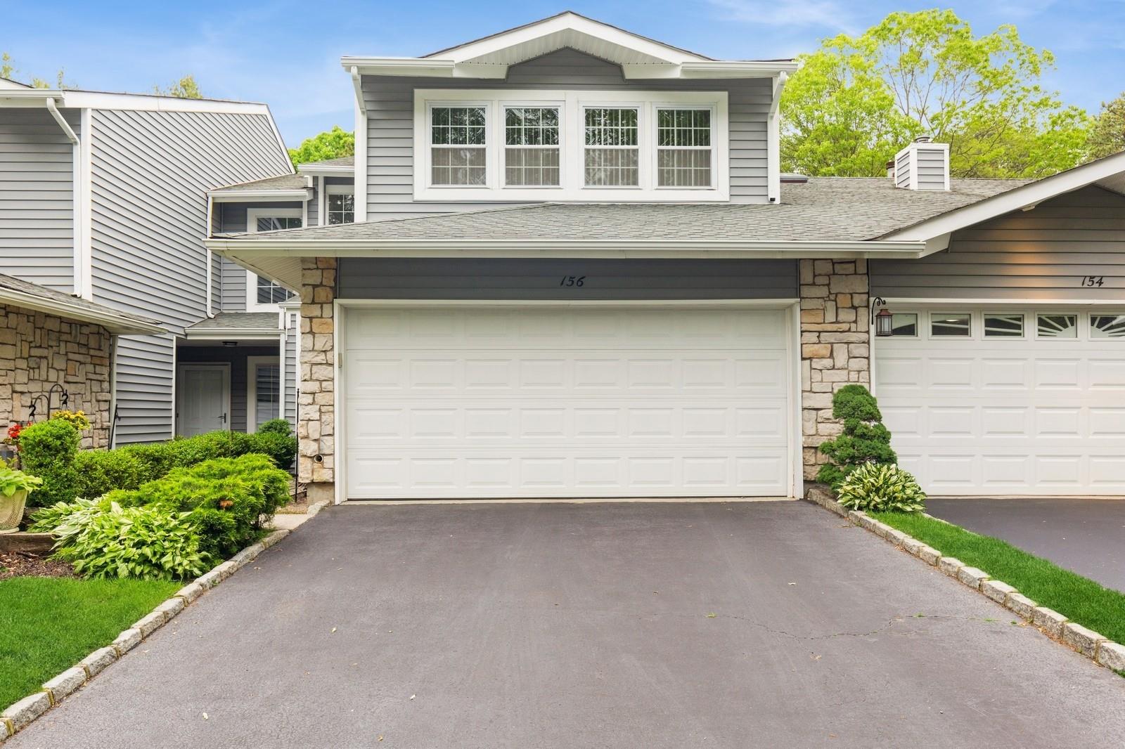 View of front of home featuring stone siding, asphalt driveway, and roof with shingles