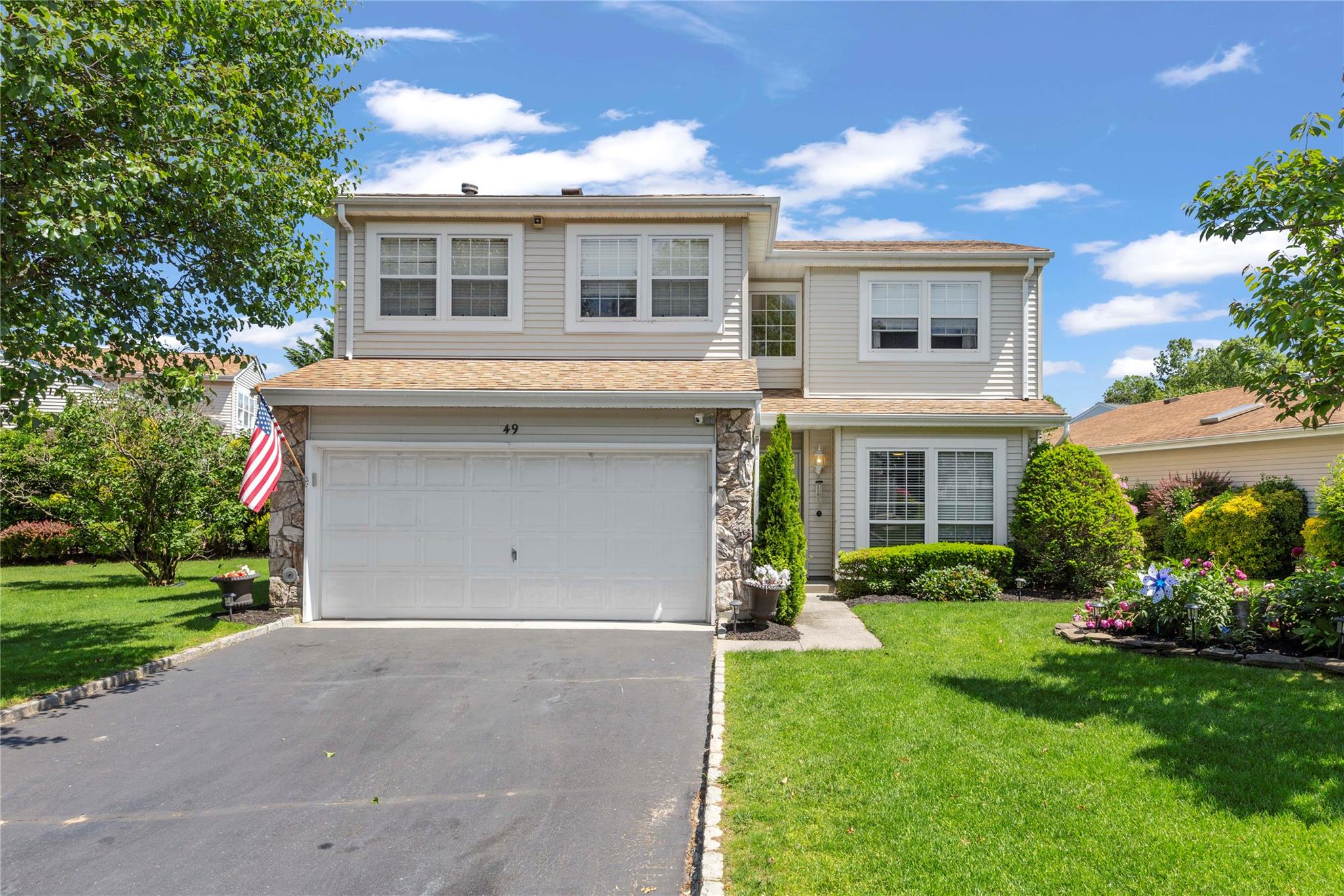 View of front facade featuring asphalt driveway, a garage, a front lawn, and stone siding
