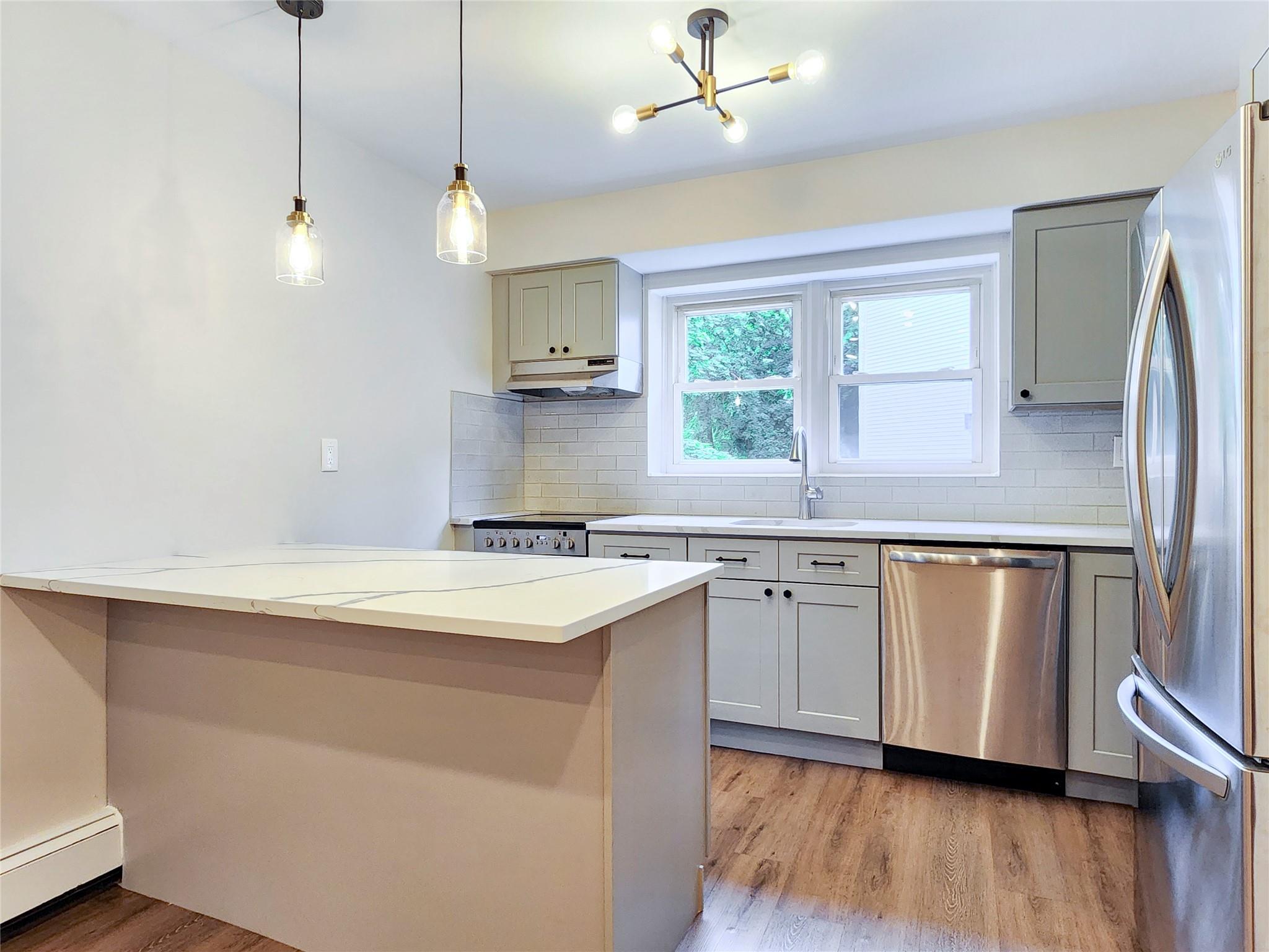 Open concept kitchen featuring modern shaker style cabinets, stainless steel appliances, quartz counter tops, modern light fixtures and large window.