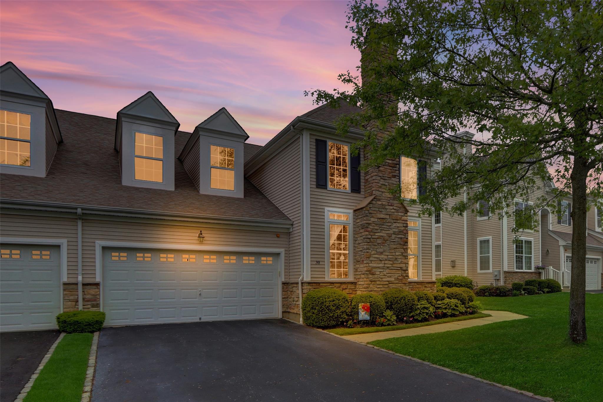 View of front of home featuring - stone siding, asphalt driveway, a yard, and a shingled roofTwilight enhanced