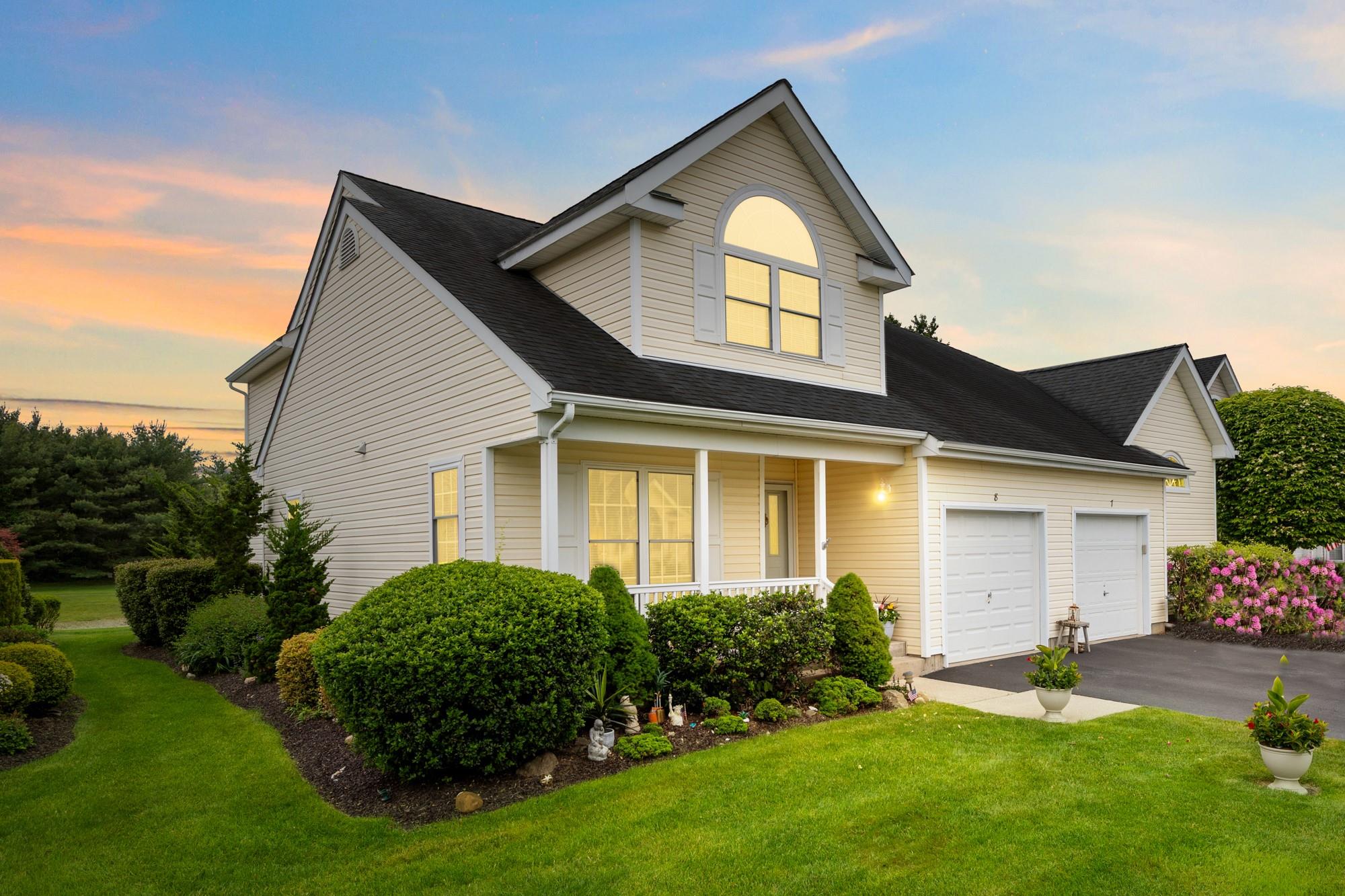 Traditional town home with an attached garage, driveway, a front yard, roof with shingles, porch and rear patio with a water view.