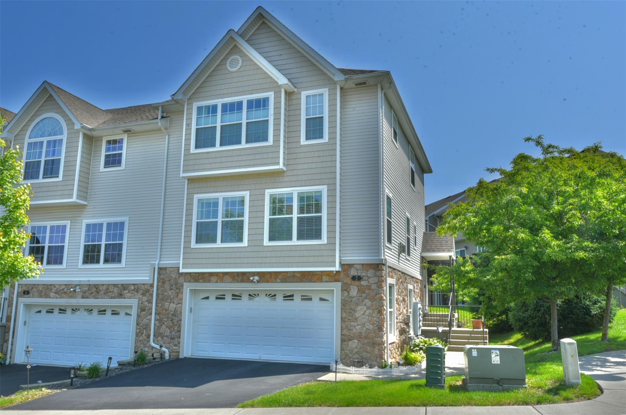 View of property with a two car garage, stone siding, and driveway