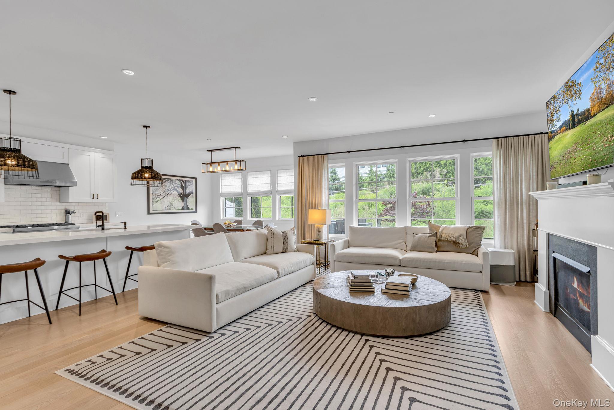 Living room featuring light white oak hardwood flooring, recessed lighting, and a glass covered fireplace