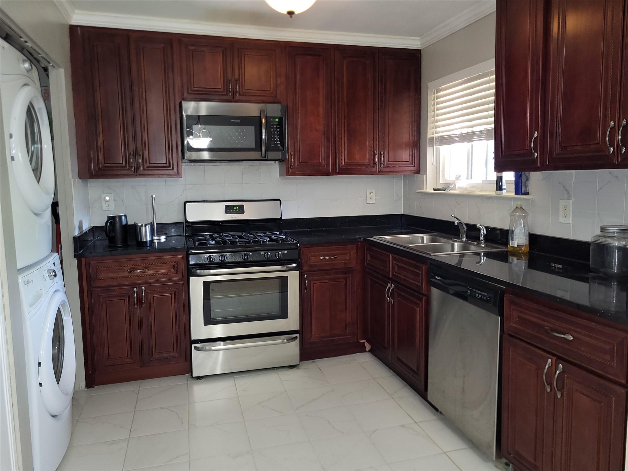 Kitchen with appliances with stainless steel finishes, reddish brown cabinets, estacked washer and dryer, a sink, and ornamental molding