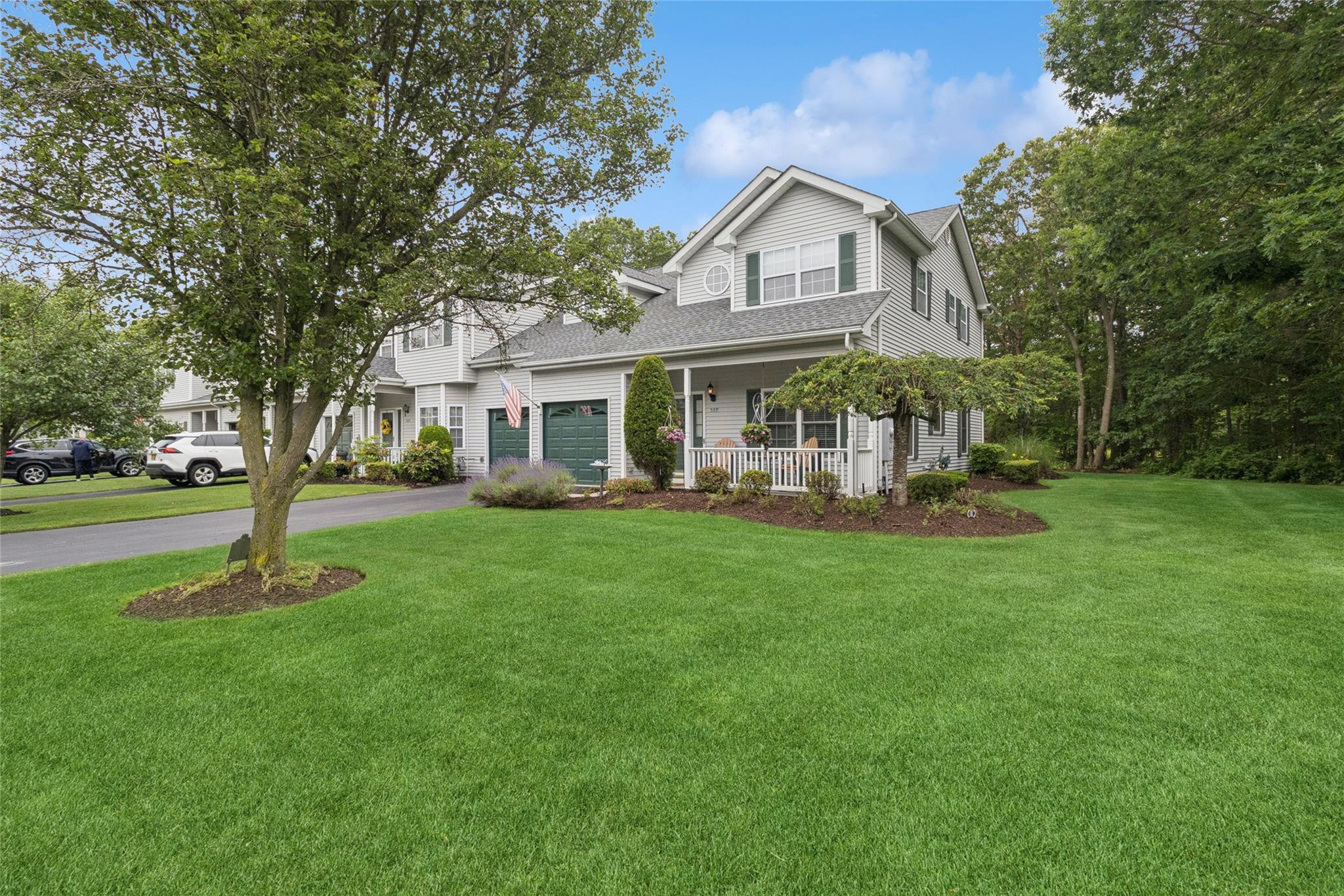 Front of home featuring a 2-car garage, asphalt driveway, covered porch, lawn and gardens.