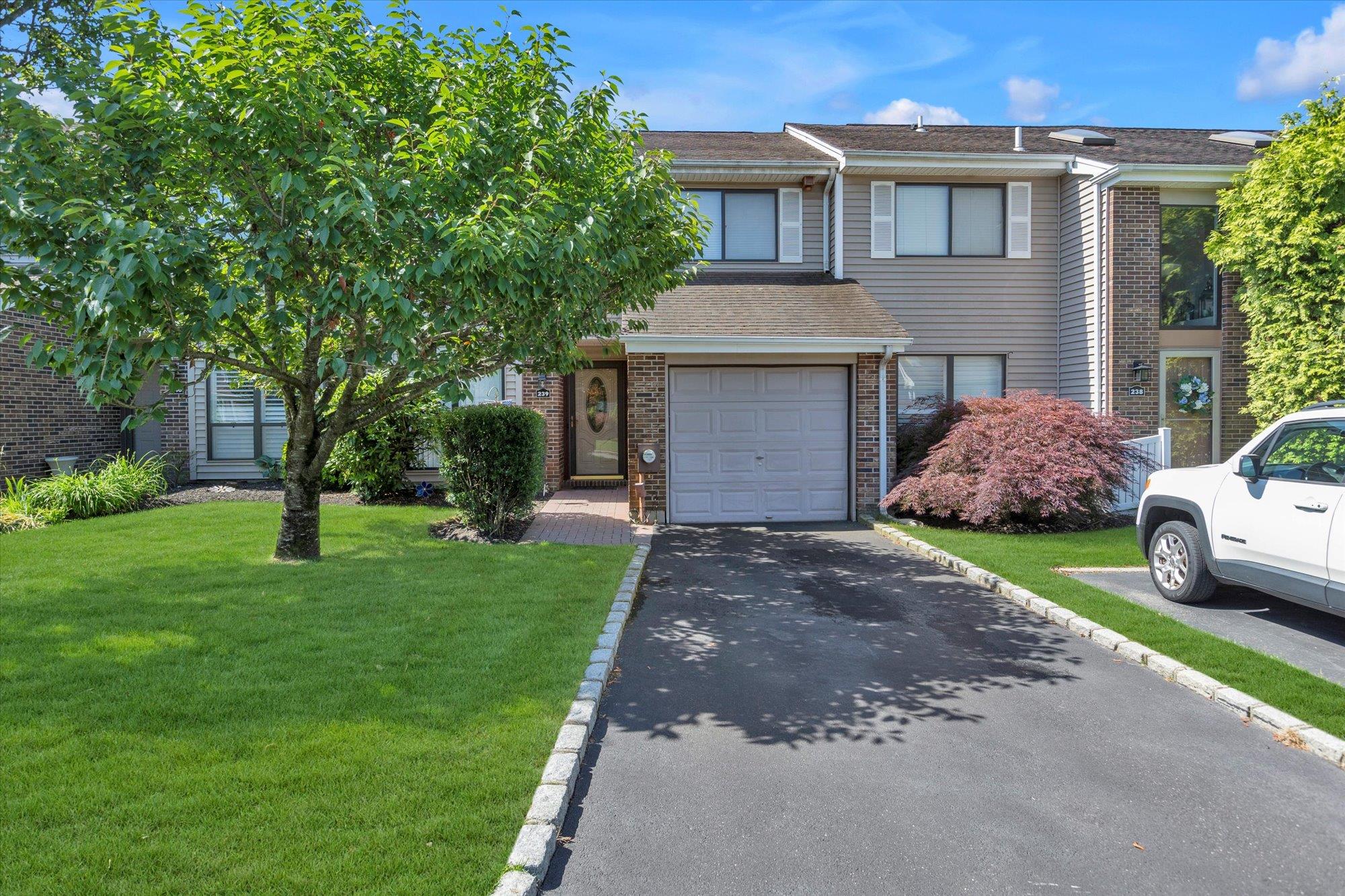 View of property featuring asphalt driveway, a front lawn, brick siding, an attached garage, and a shingled roof