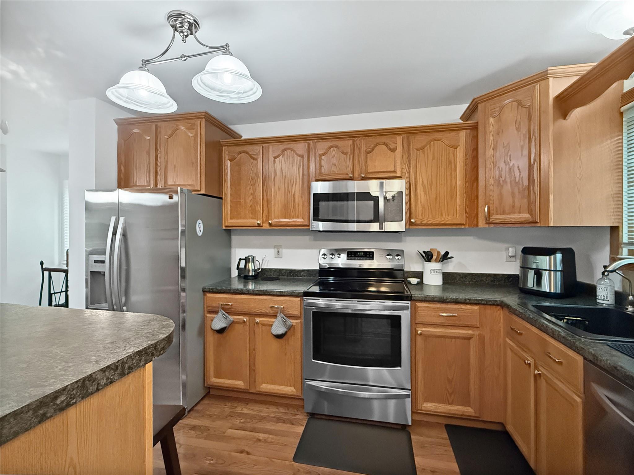 Kitchen with stainless steel appliances, dark countertops, and light wood-type flooring