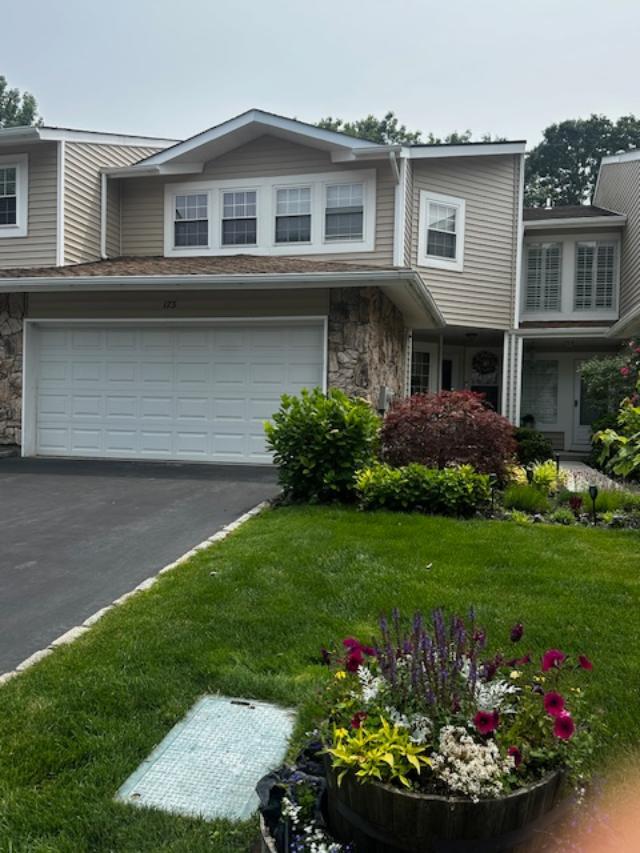 Townhome / multi-family property featuring stone siding, asphalt driveway, an attached garage, and a front yard