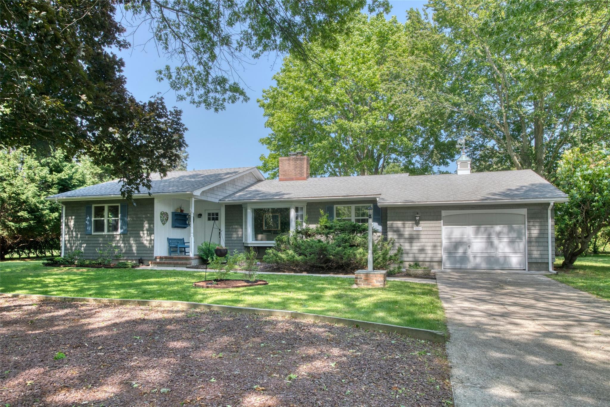 Single story home with a chimney, a garage, concrete driveway, and a front lawn