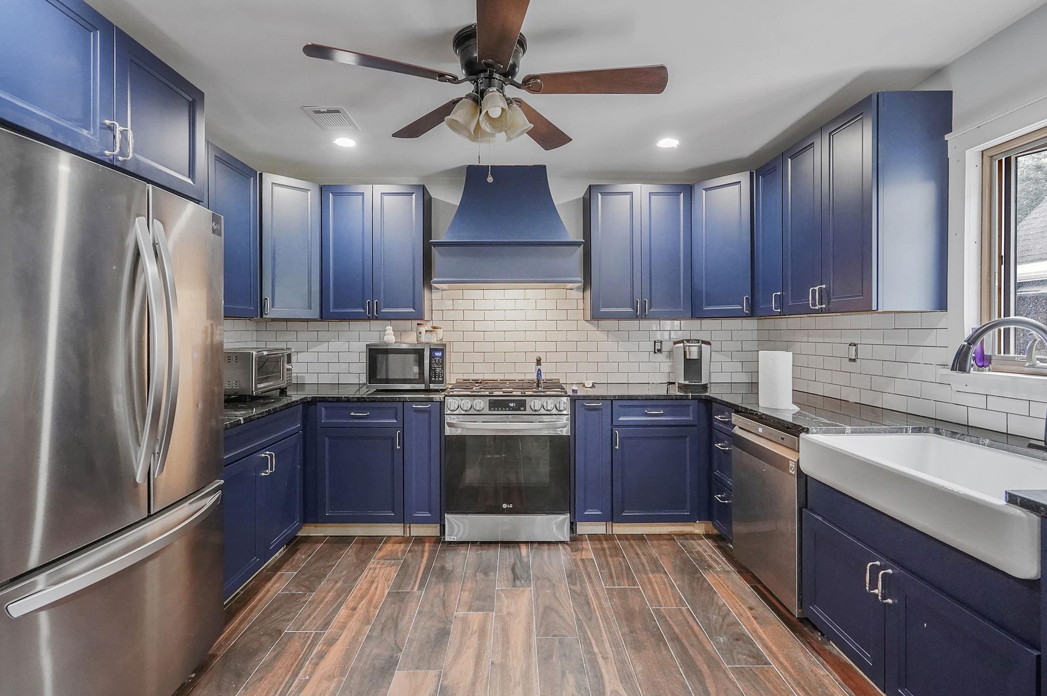 Kitchen featuring stainless steel appliances, premium range hood, blue cabinetry, and ceiling fan