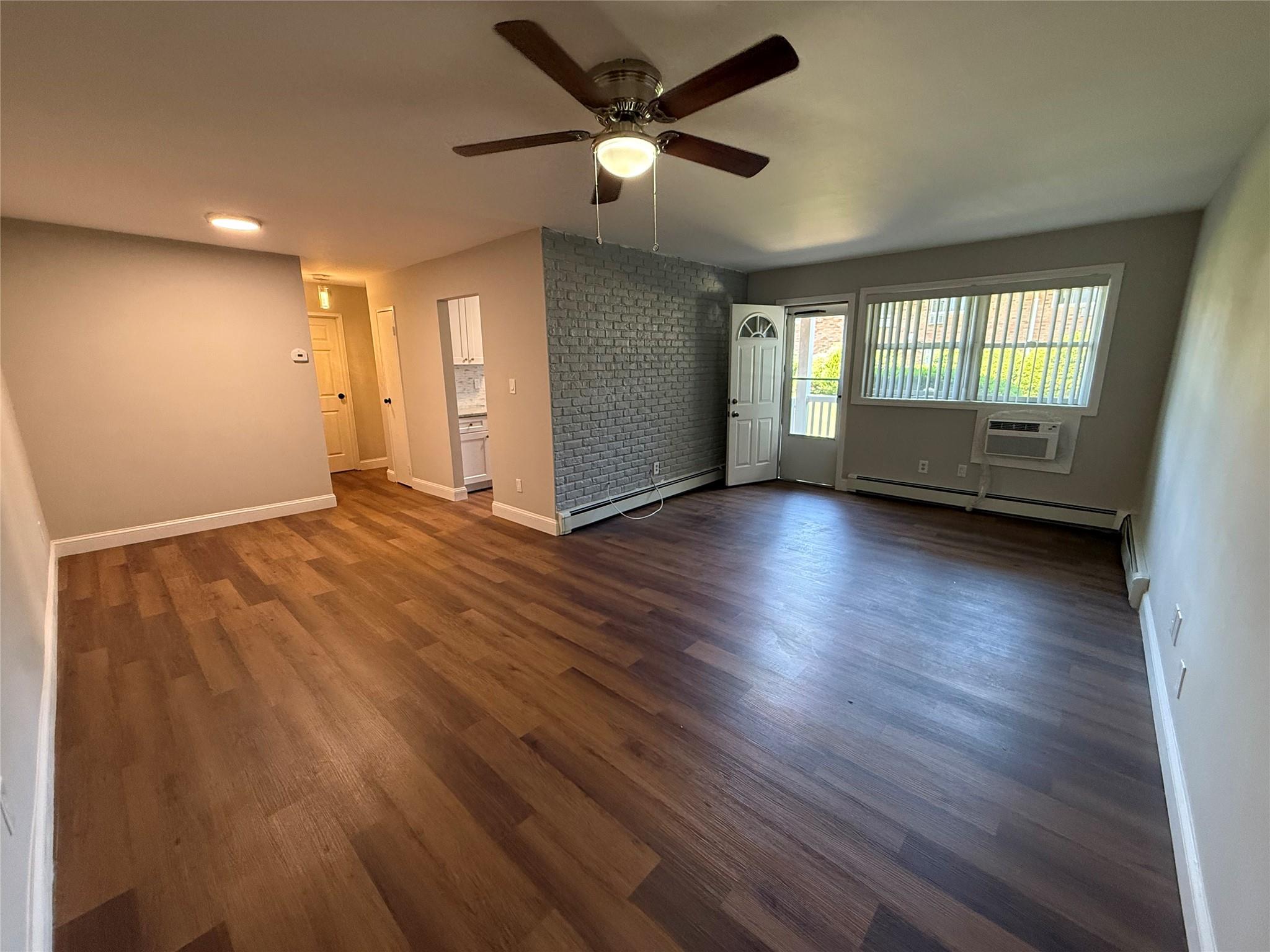 Spare room featuring a ceiling fan, an AC wall unit, a baseboard heating unit, and dark wood-style flooring