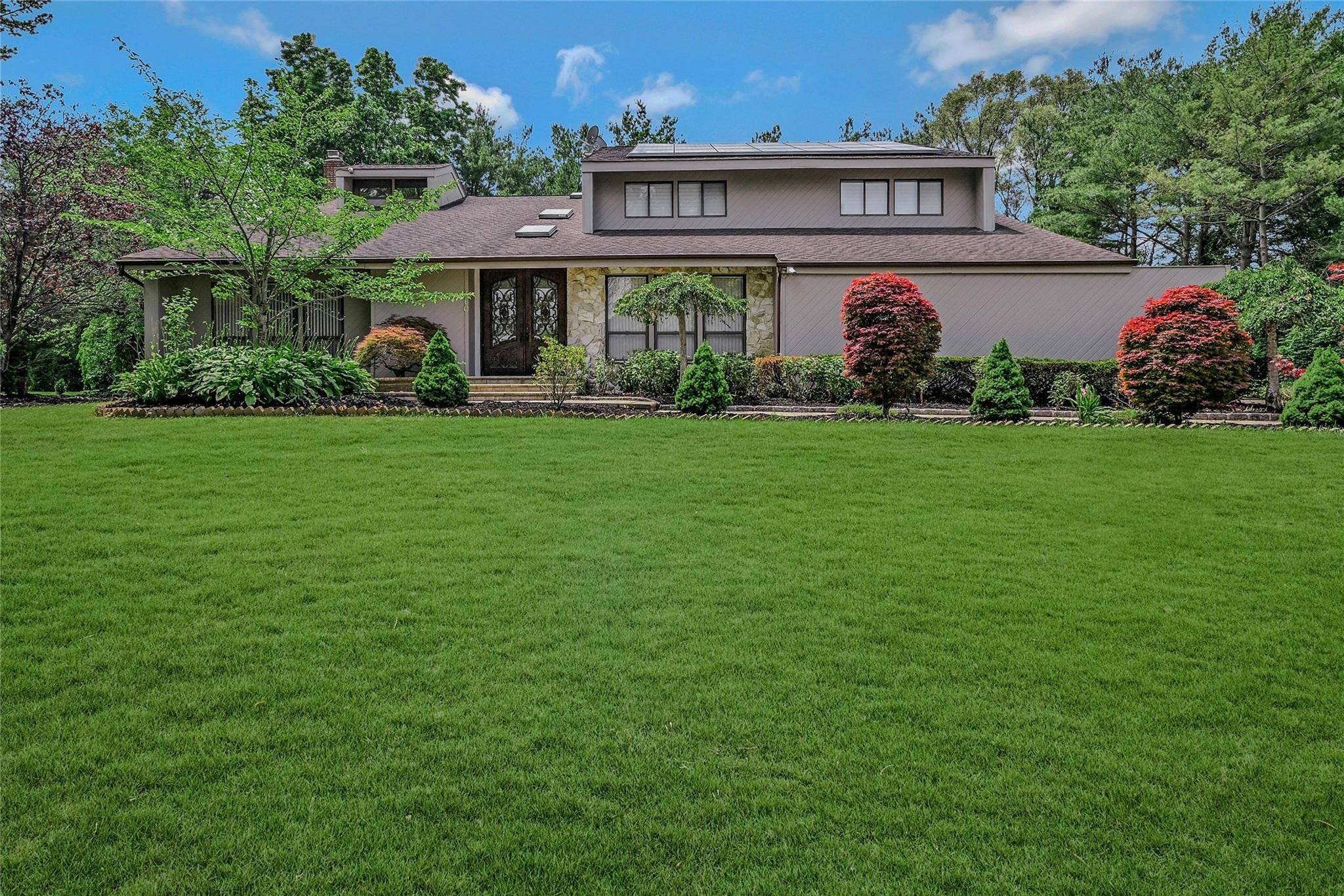 View of front facade featuring roof mounted solar panels, a front lawn, and roof with shingles