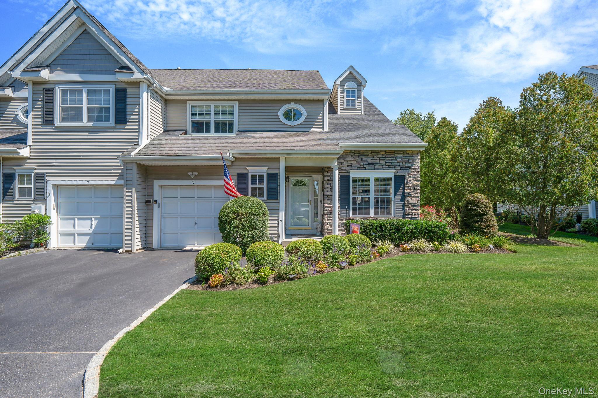 View of front of home with driveway, a front yard, an attached garage, stone siding, and roof with shingles