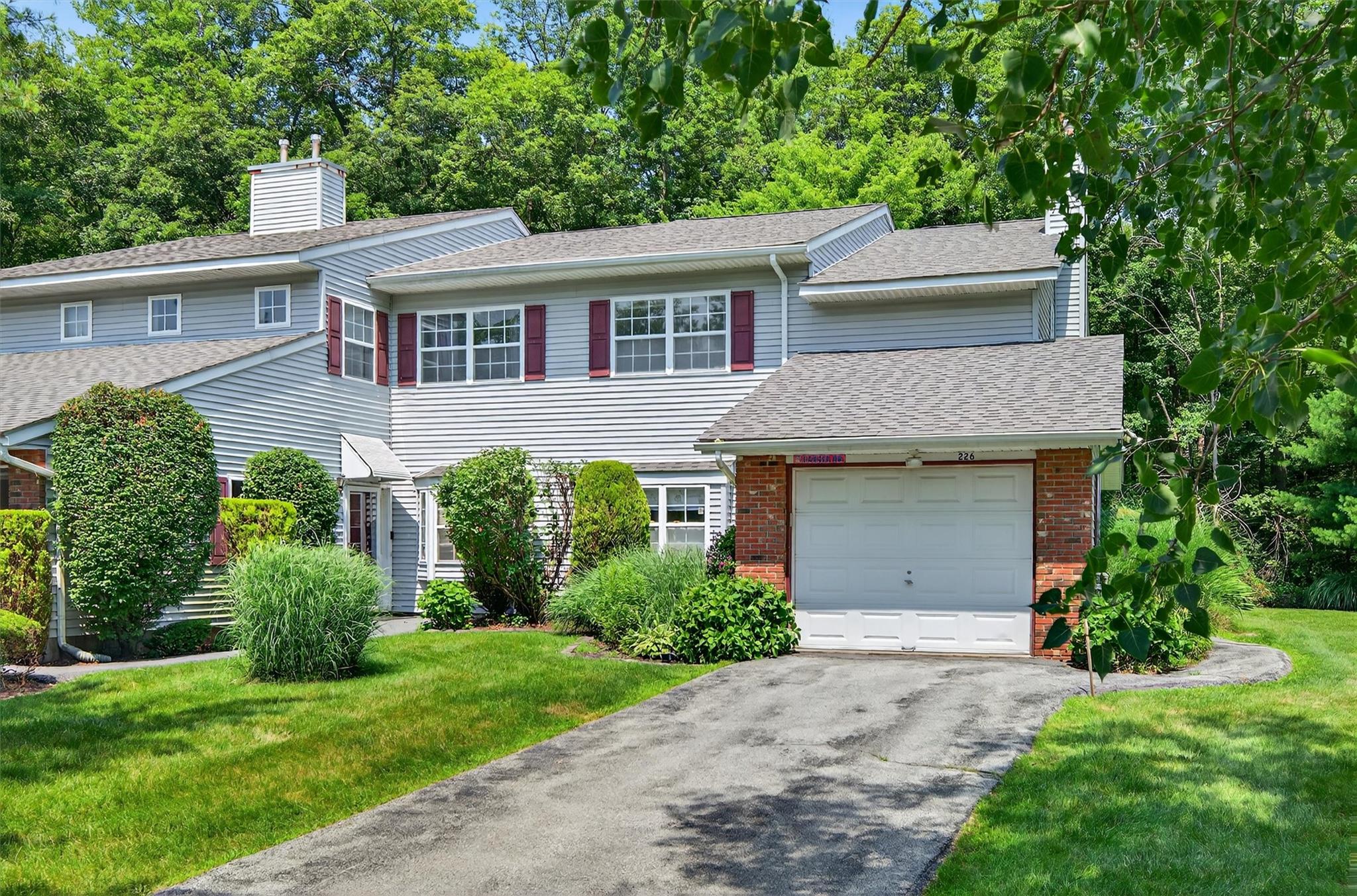 View of property with an attached garage, a front lawn, driveway, brick siding, and roof with shingles