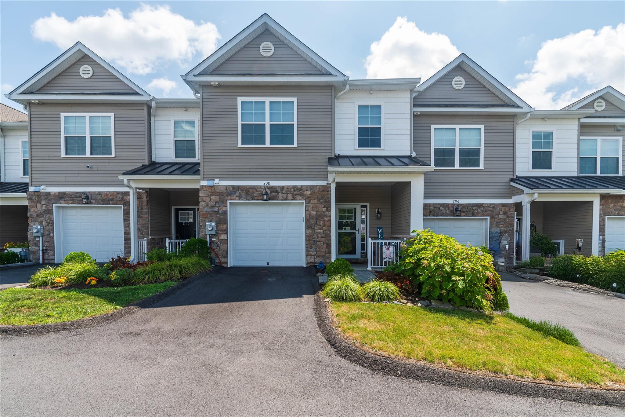 Townhome property featuring stone siding,  an attached garage, and driveway