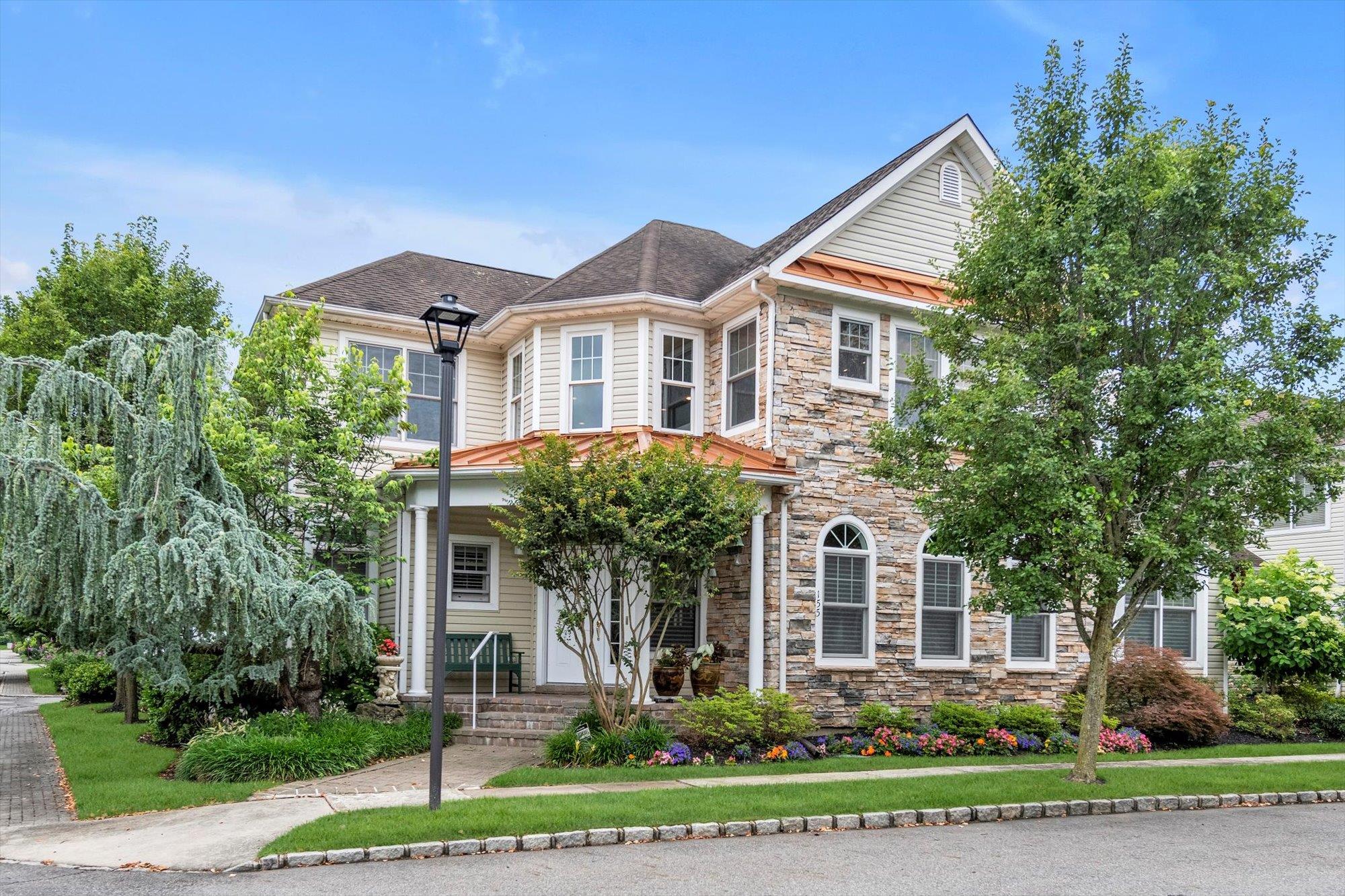 View of front facade featuring stone siding, a shingled roof, and covered porch  Custom landscaping throughout