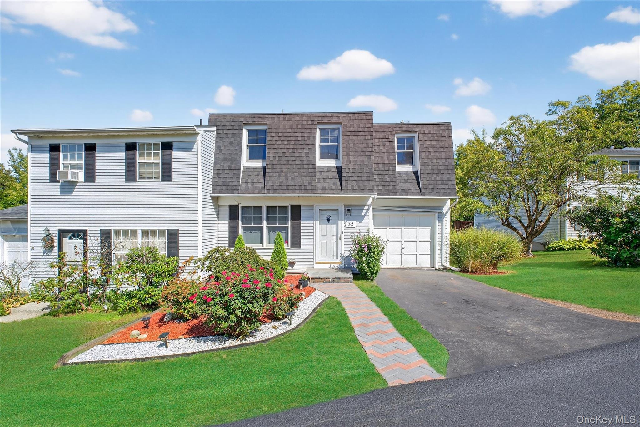 View of property featuring a front yard, roof with shingles, mansard roof, driveway, and a garage