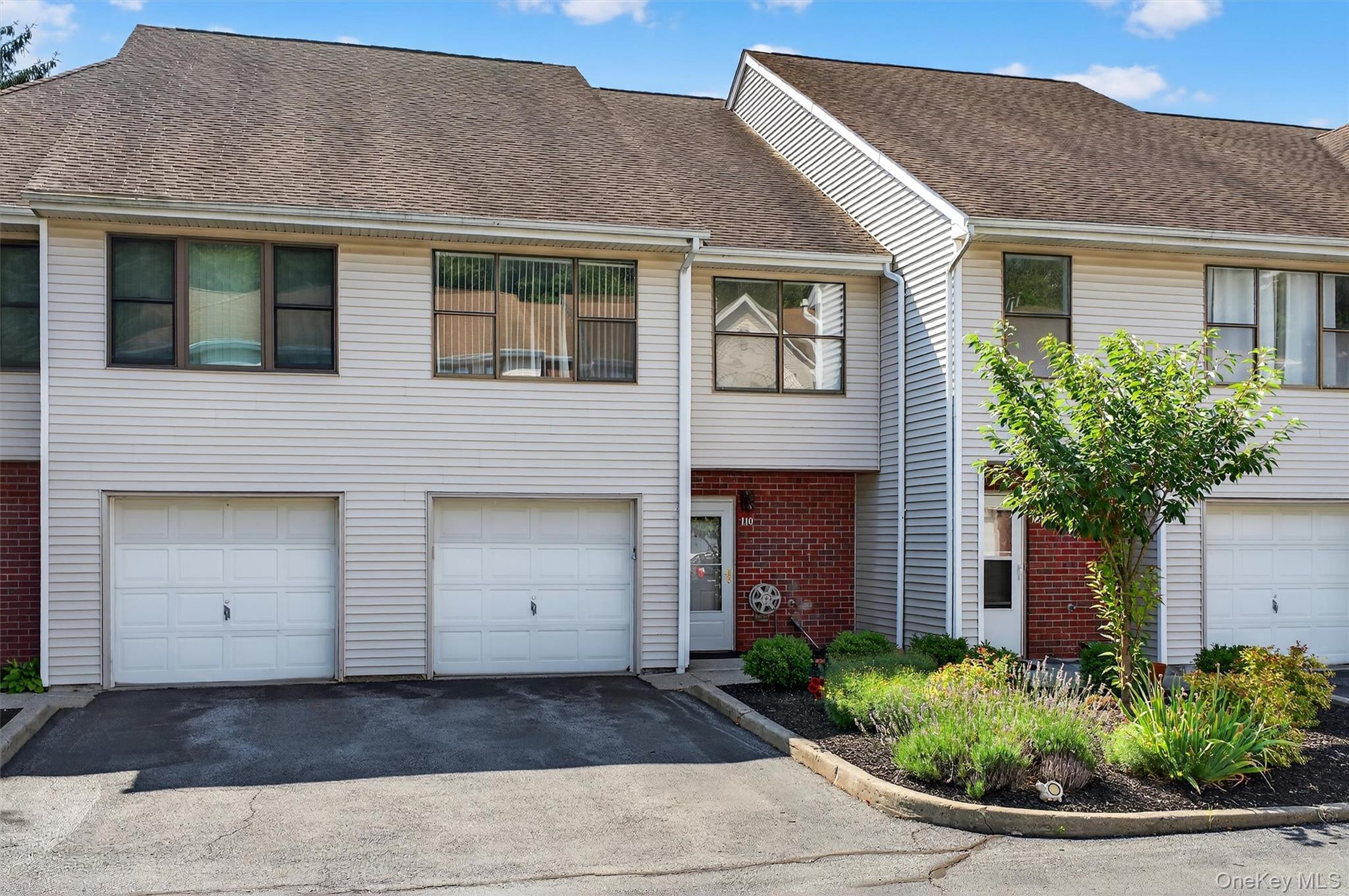 View of front of property with driveway, a garage, a shingled roof, and brick siding