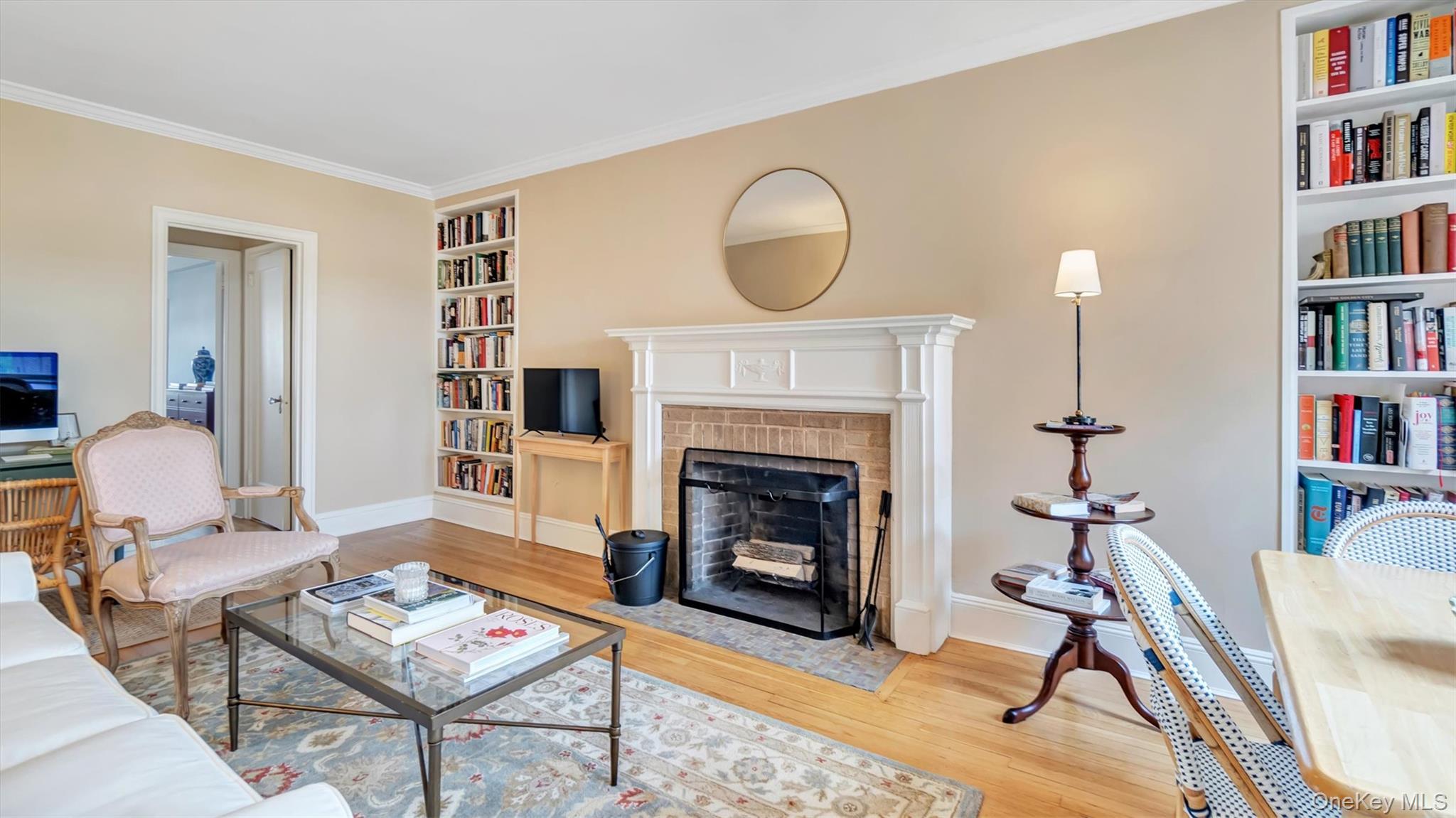 Living room with built in features, wood finished floors, baseboards, crown molding, and a fireplace with flush hearth