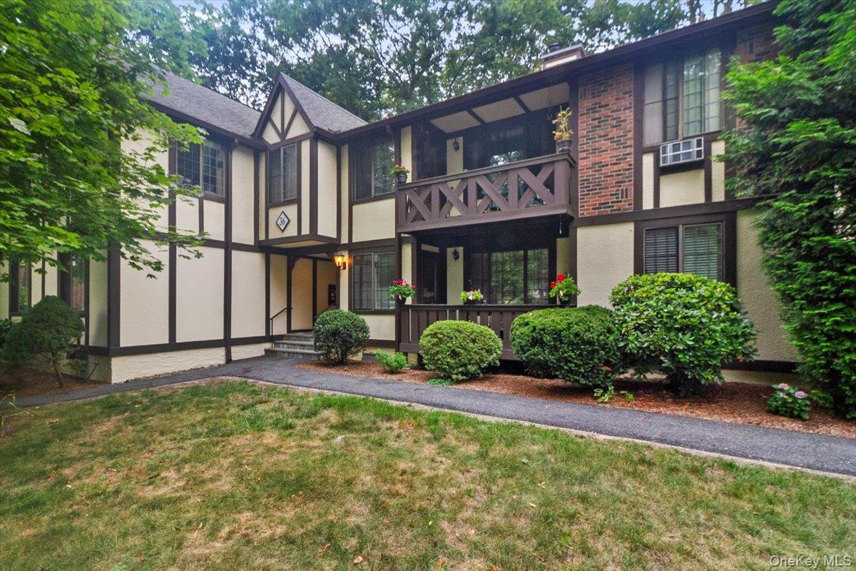Tudor-style house with stucco siding, a balcony, a front yard, and a chimney