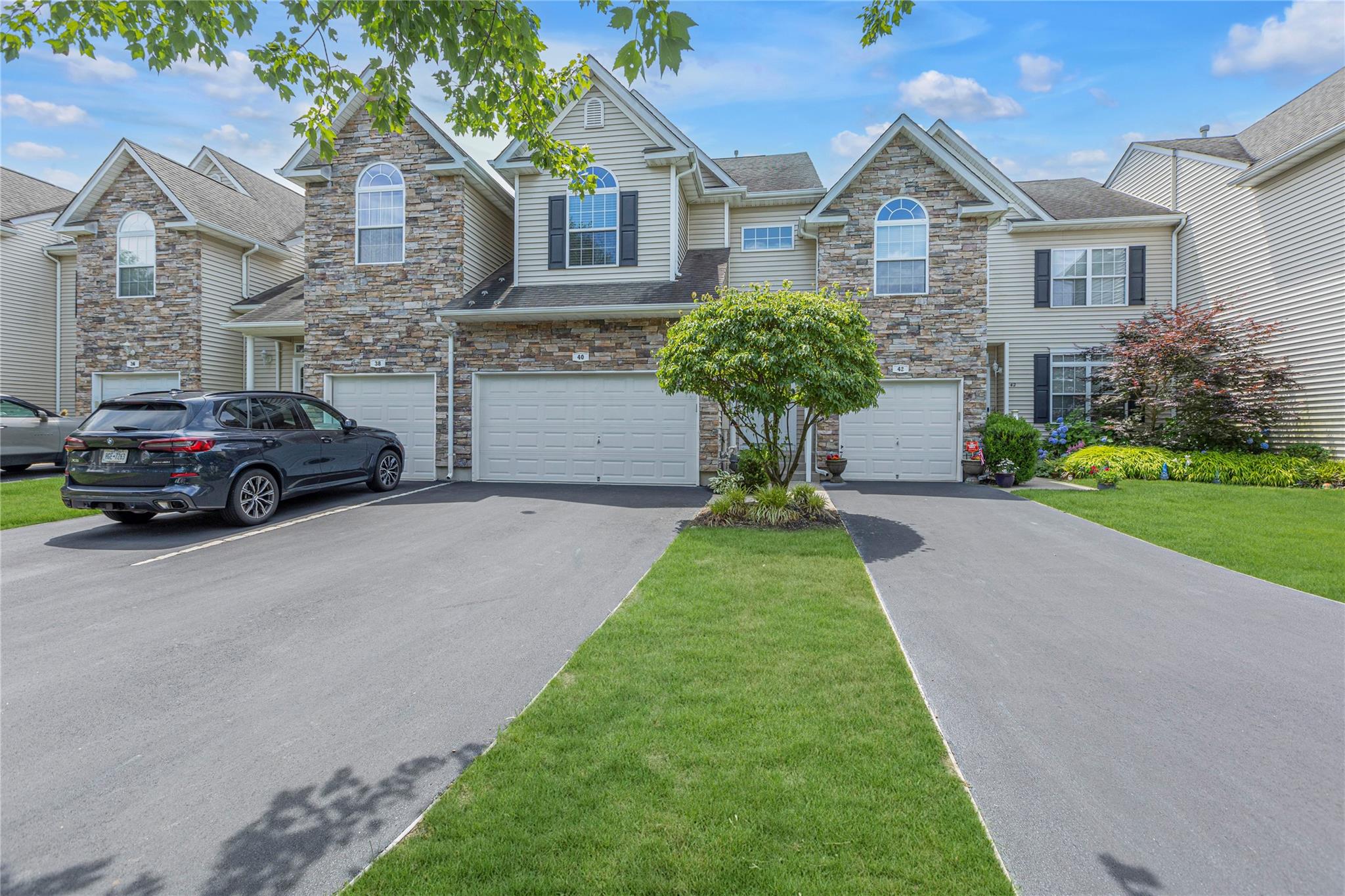 View of front of property featuring driveway, an attached garage, stone siding, and a front lawn
