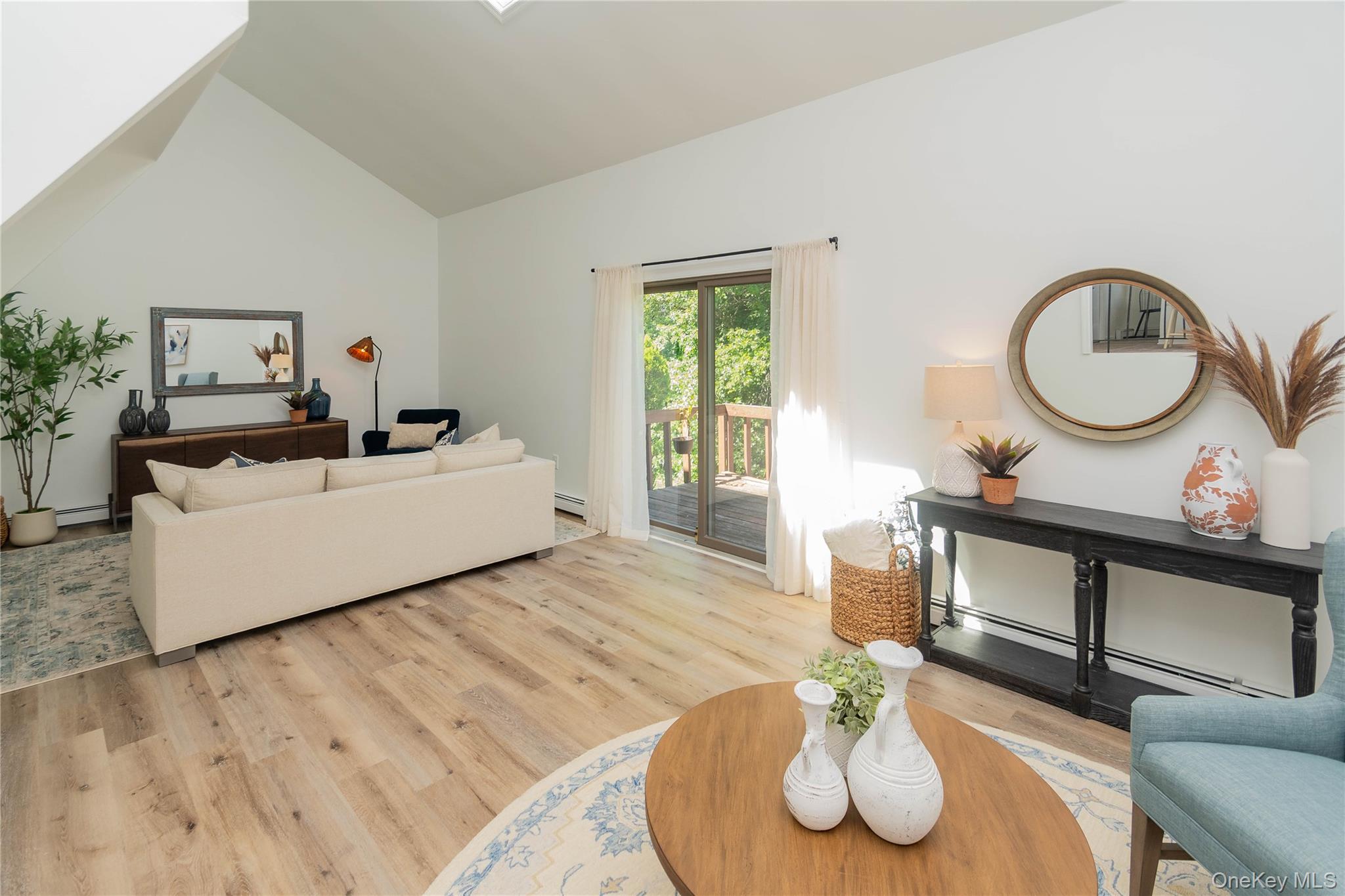 Living area featuring vaulted ceiling, a skylight, light wood-style floors, and a baseboard radiator