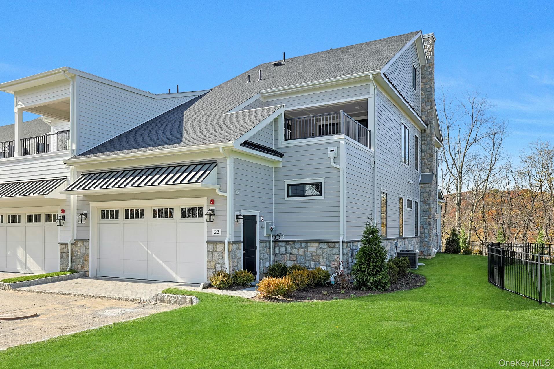 Back of house featuring a balcony, stone siding, a garage, and driveway