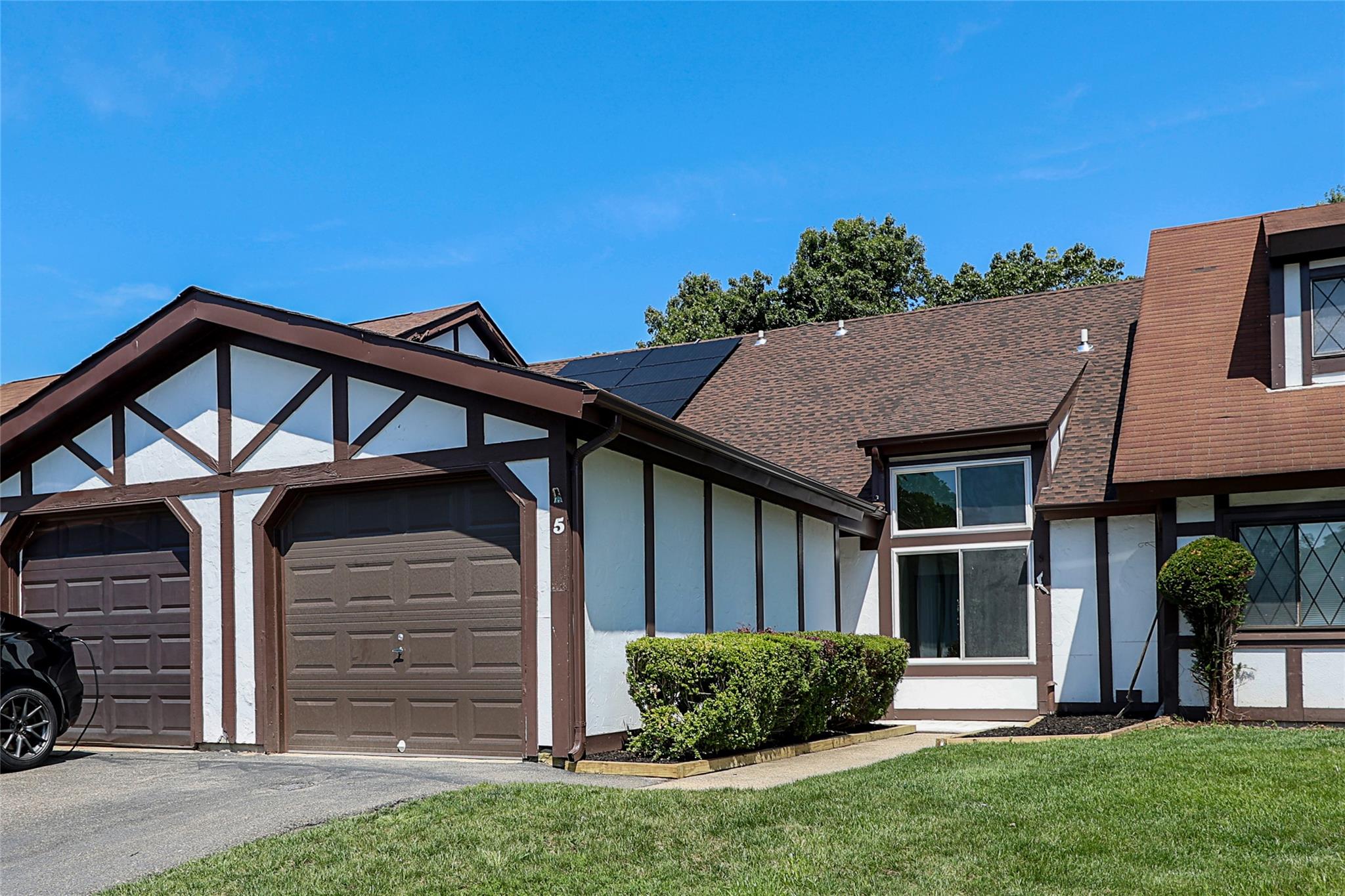 Tudor house with a shingled roof, a front yard, a garage, solar panels, and asphalt driveway