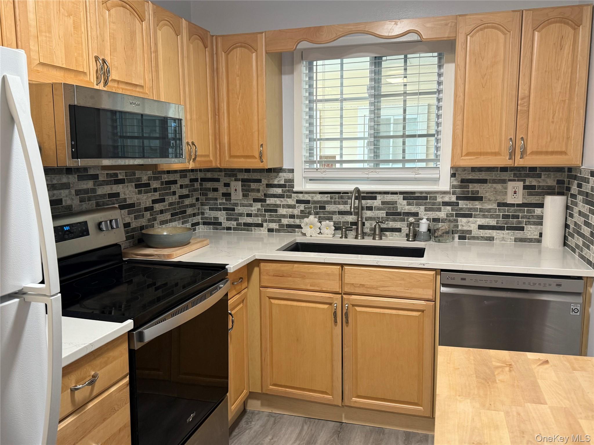Kitchen with stainless steel appliances, light countertops, tasteful backsplash, and light brown cabinets