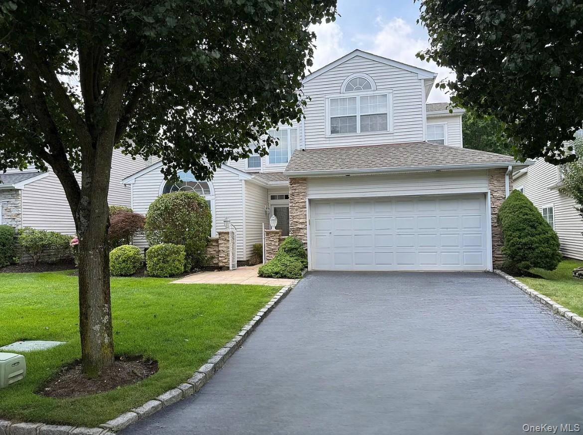View of front of home with stone siding, roof with shingles, asphalt driveway, an attached garage, and a front lawn