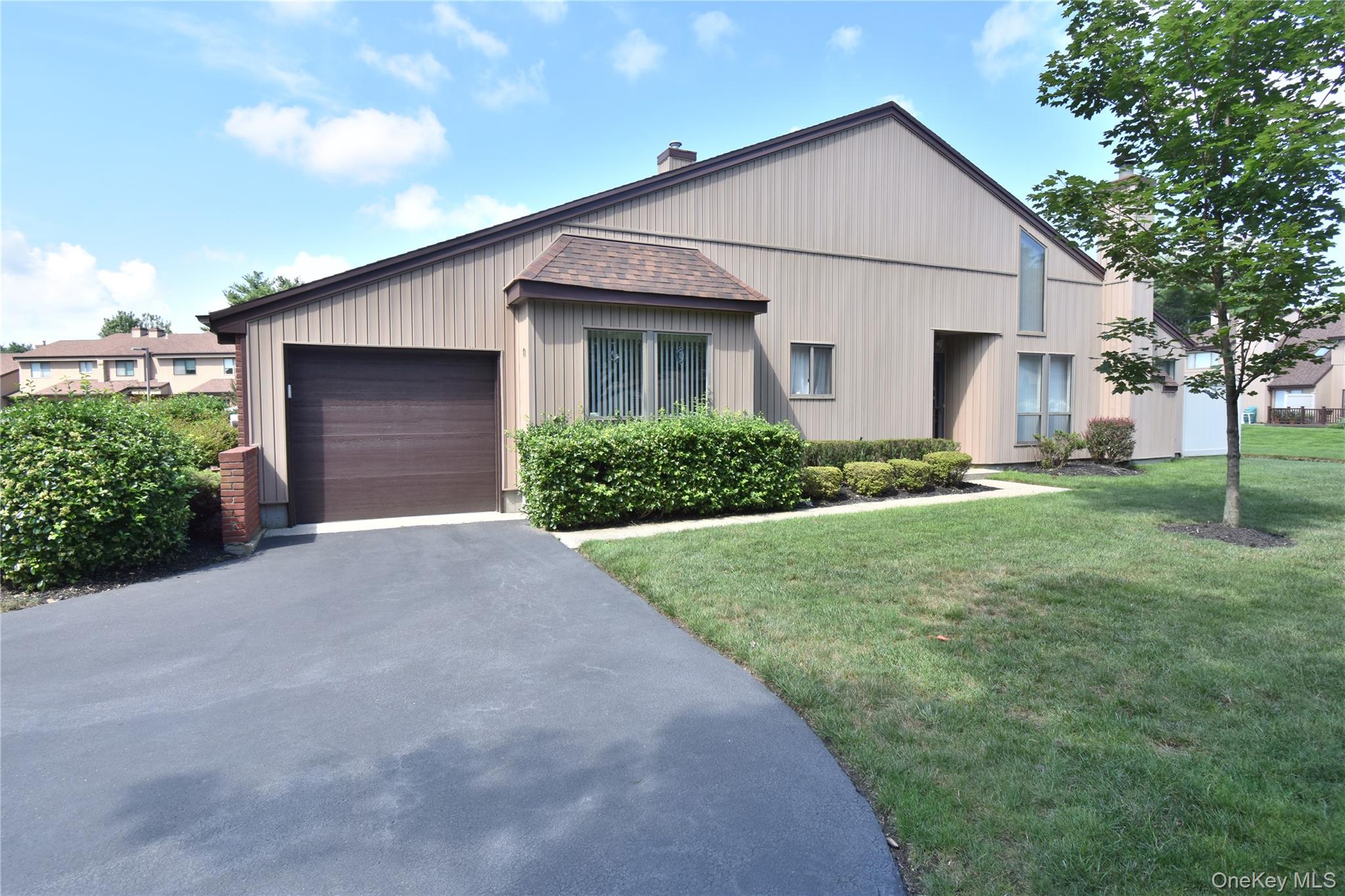 View of front of house featuring a front lawn, driveway, a garage, and roof with shingles