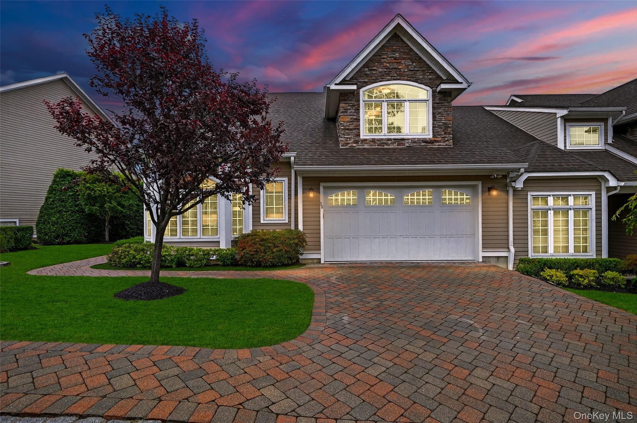 Traditional-style home featuring decorative driveway, a yard, a shingled roof, an attached garage, and stone siding