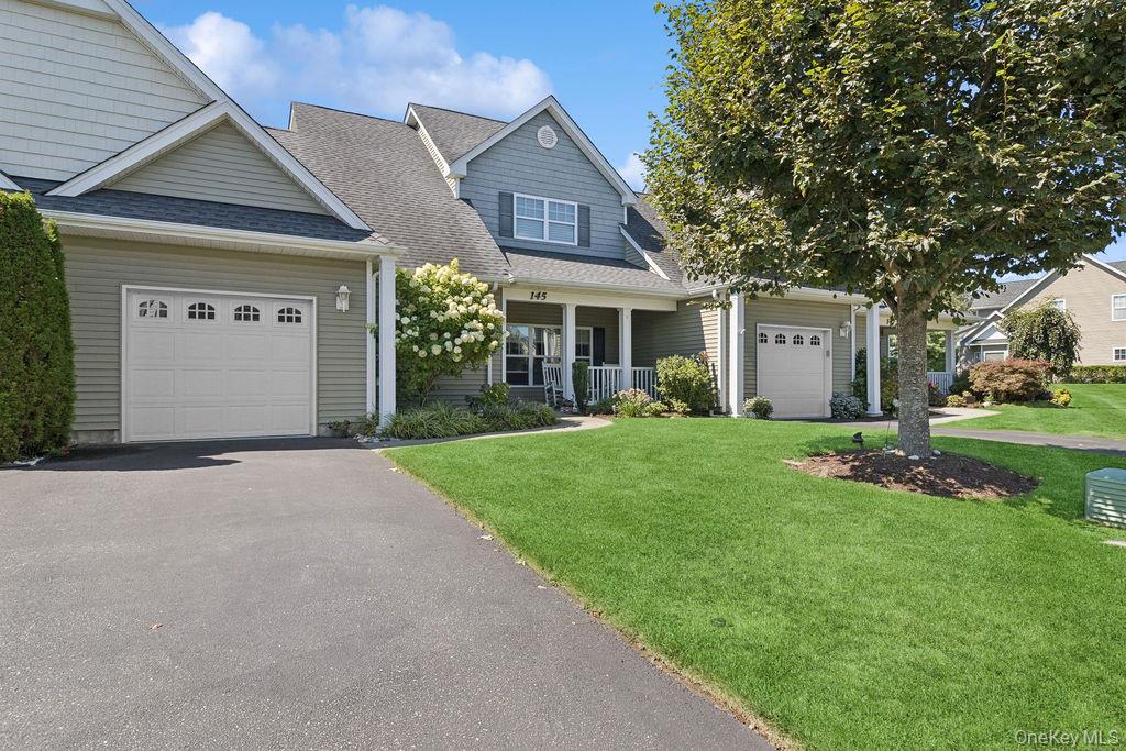 View of front of home featuring a porch, a shingled roof, asphalt driveway, a front yard, and an attached garage