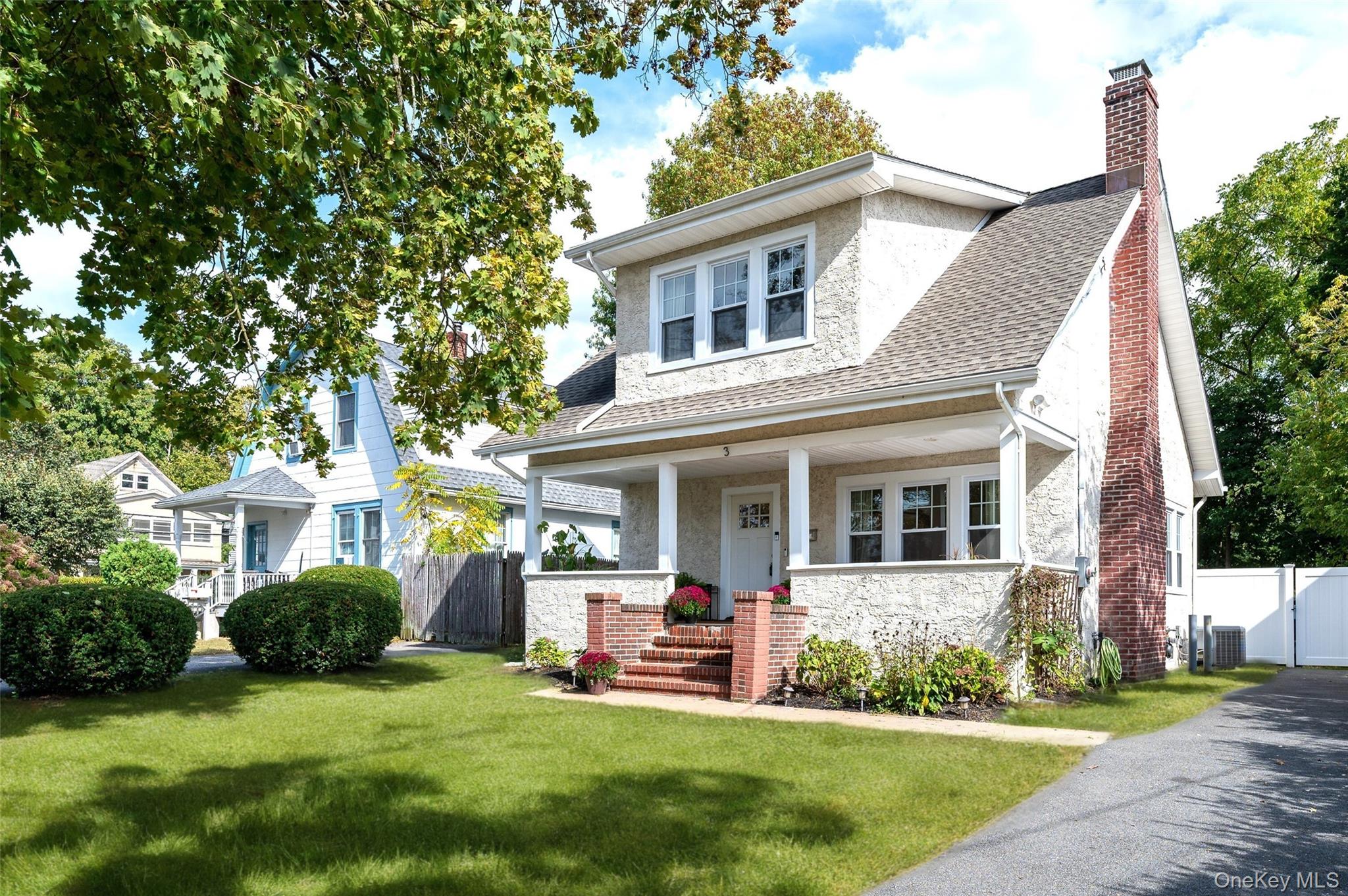 View of front of house with a chimney, a porch, stucco siding, and a shingled roof