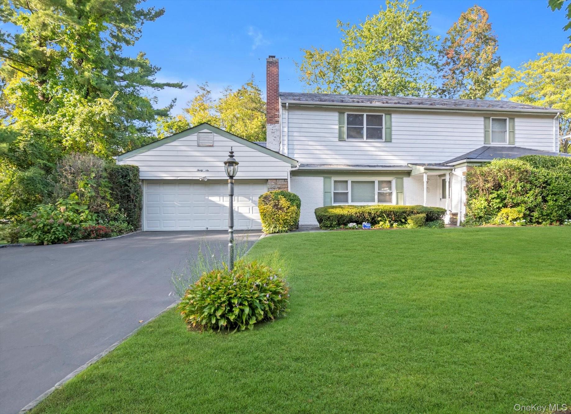 View of front facade with driveway, a chimney, a front lawn, a garage, and brick siding