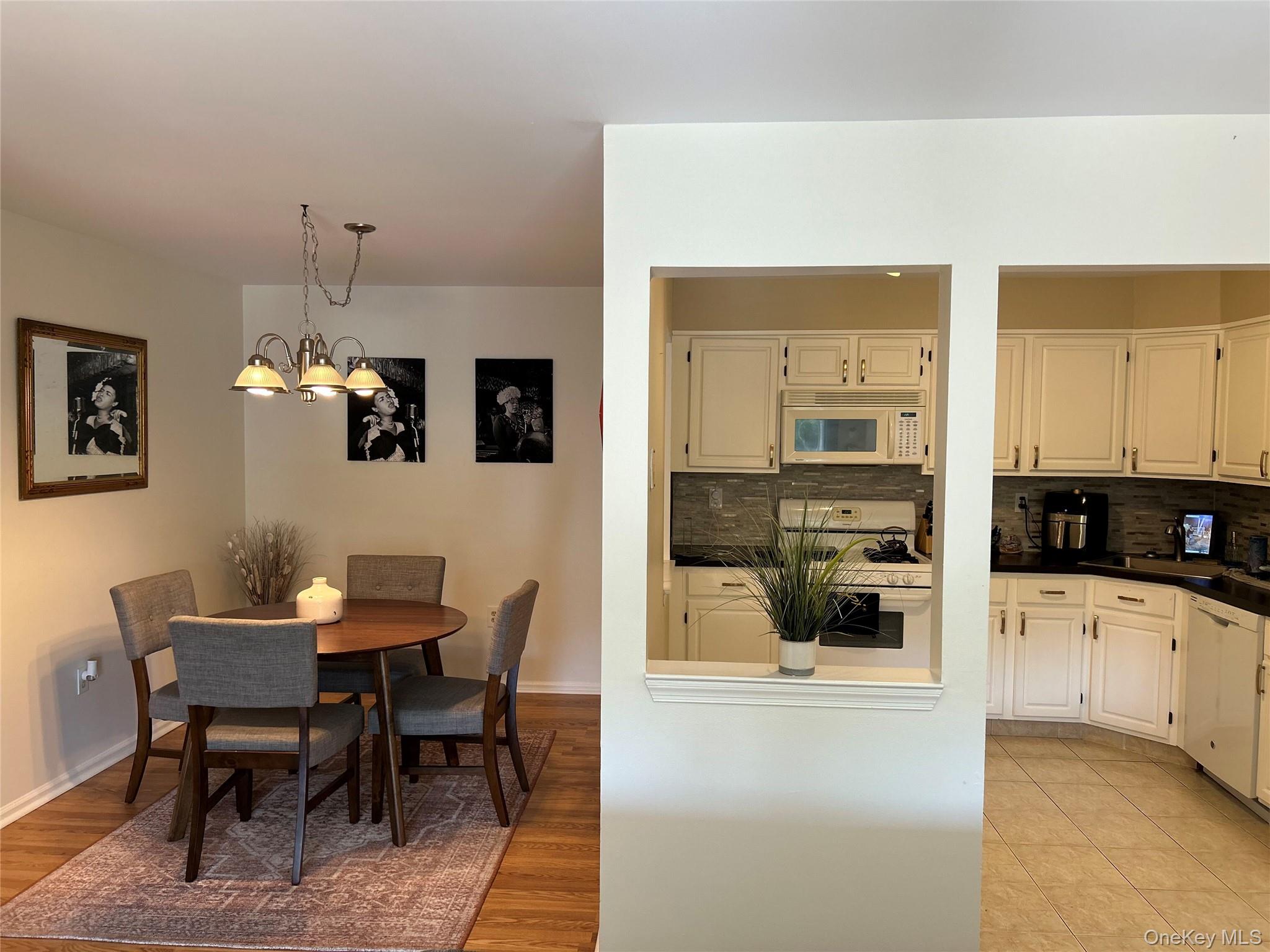 Kitchen with dark countertops, white appliances, backsplash, hanging light fixtures, and light wood-style floors
