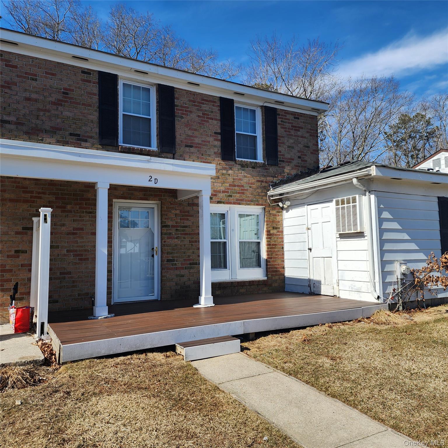 View of front of home with a deck, brick siding, and a front lawn