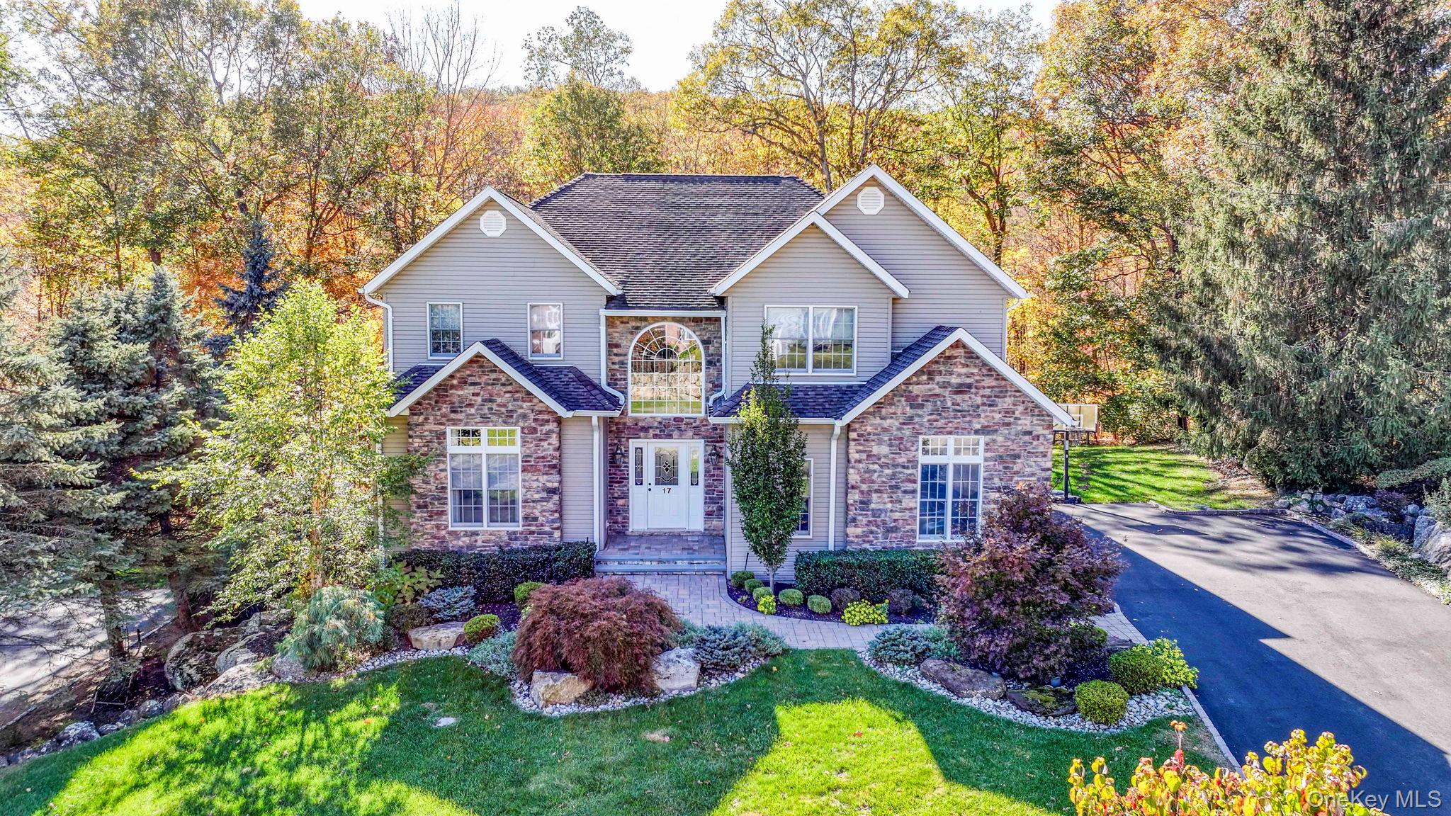 Traditional home with stone siding, a front lawn, a shingled roof, and driveway