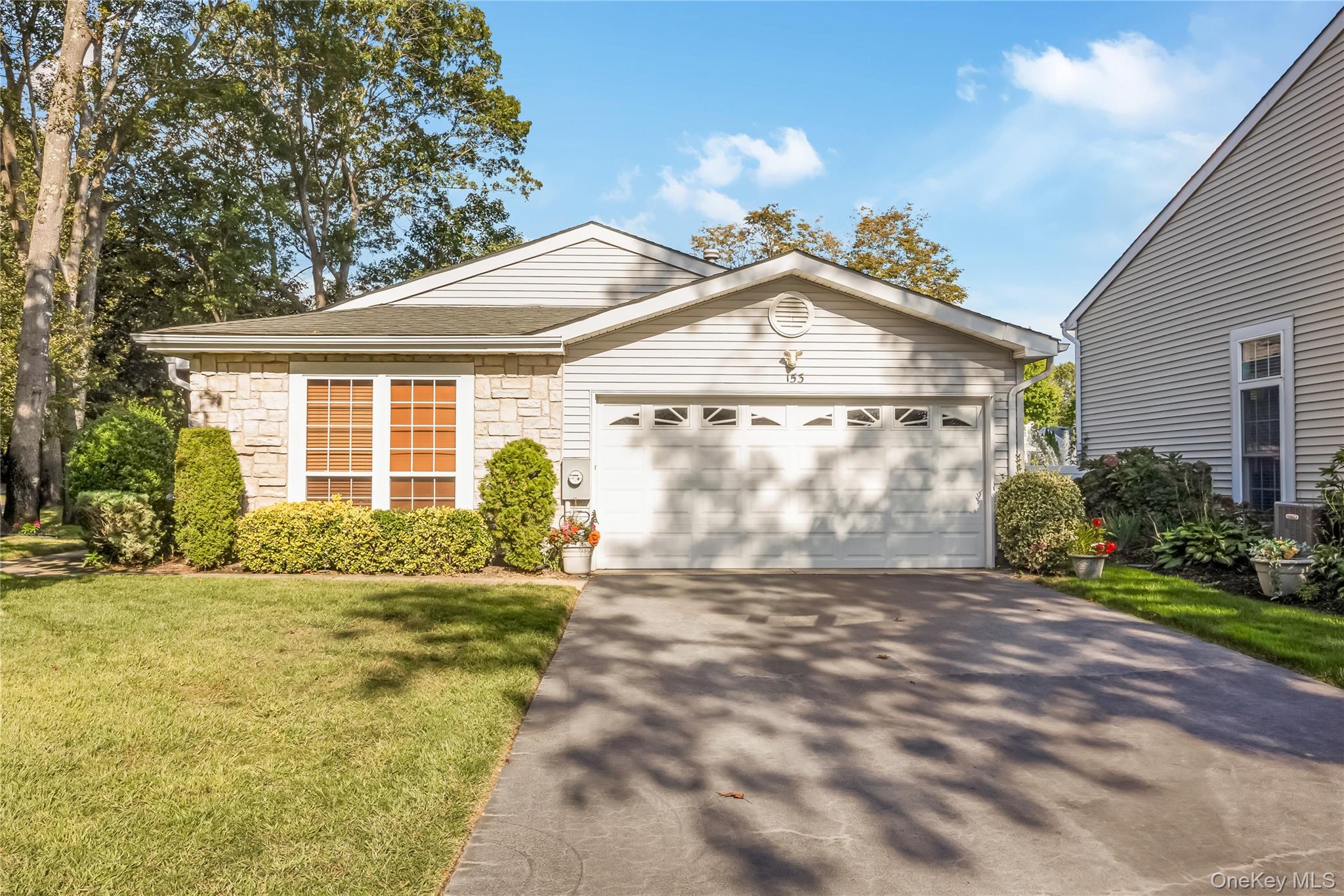 Ranch-style home featuring stone siding, driveway, a front lawn, and an attached garage