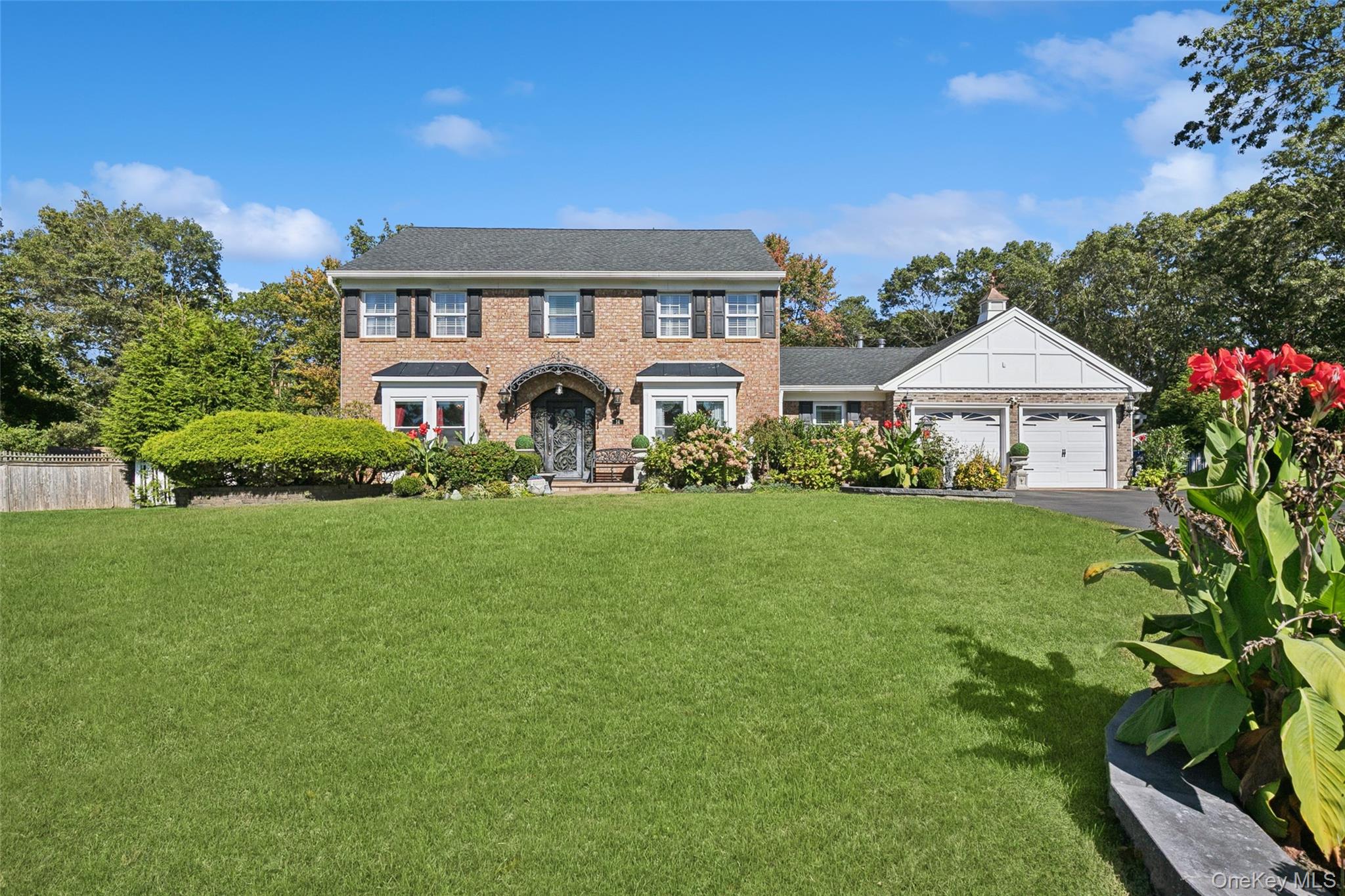 Colonial house with a front lawn, brick siding, driveway, and an attached garage