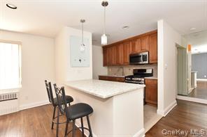 Kitchen with a kitchen bar, brown cabinetry, dark wood finished floors, light countertops, and recessed lighting