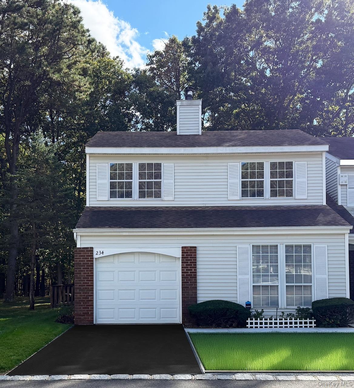 Traditional-style home with a front yard, a chimney, an attached garage, and brick siding