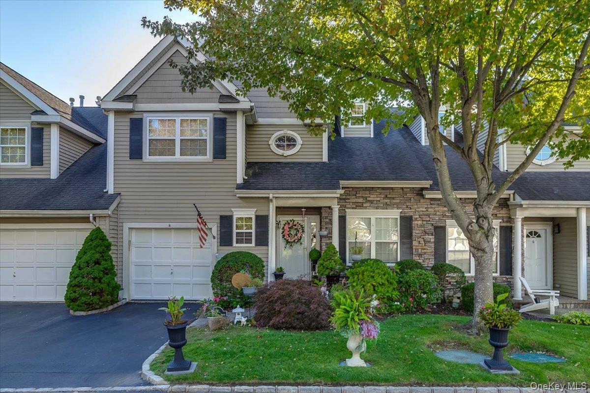 View of front of property with stone siding, asphalt driveway, a front lawn, a shingled roof, and a garage
