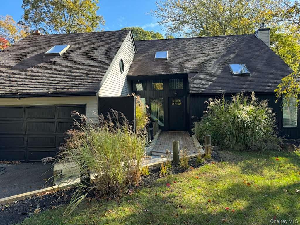 View of front of home with a chimney, a shingled roof, a garage, and a front lawn