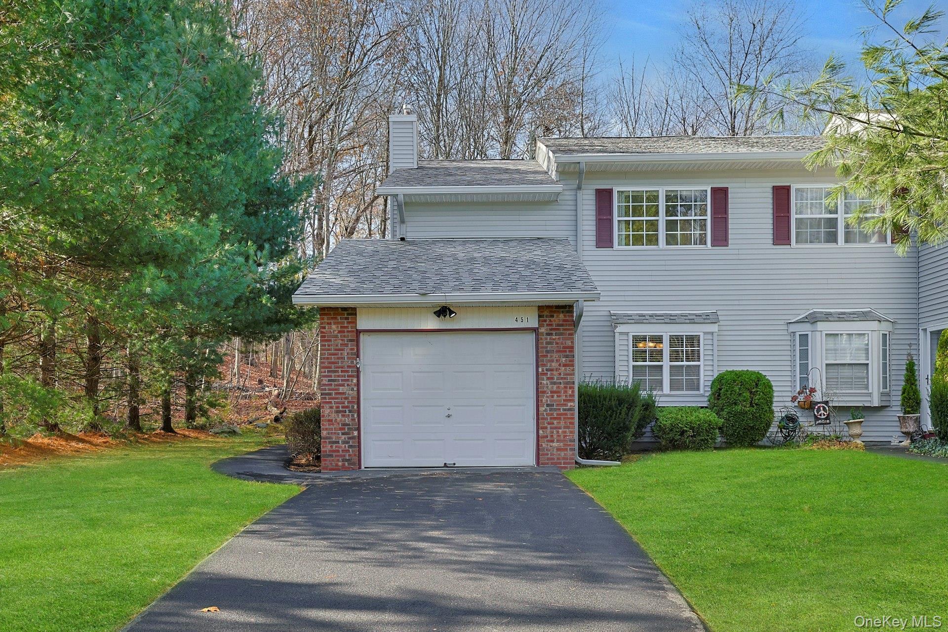 View of front of home featuring a shingled roof, a front yard, brick siding, a chimney, and driveway