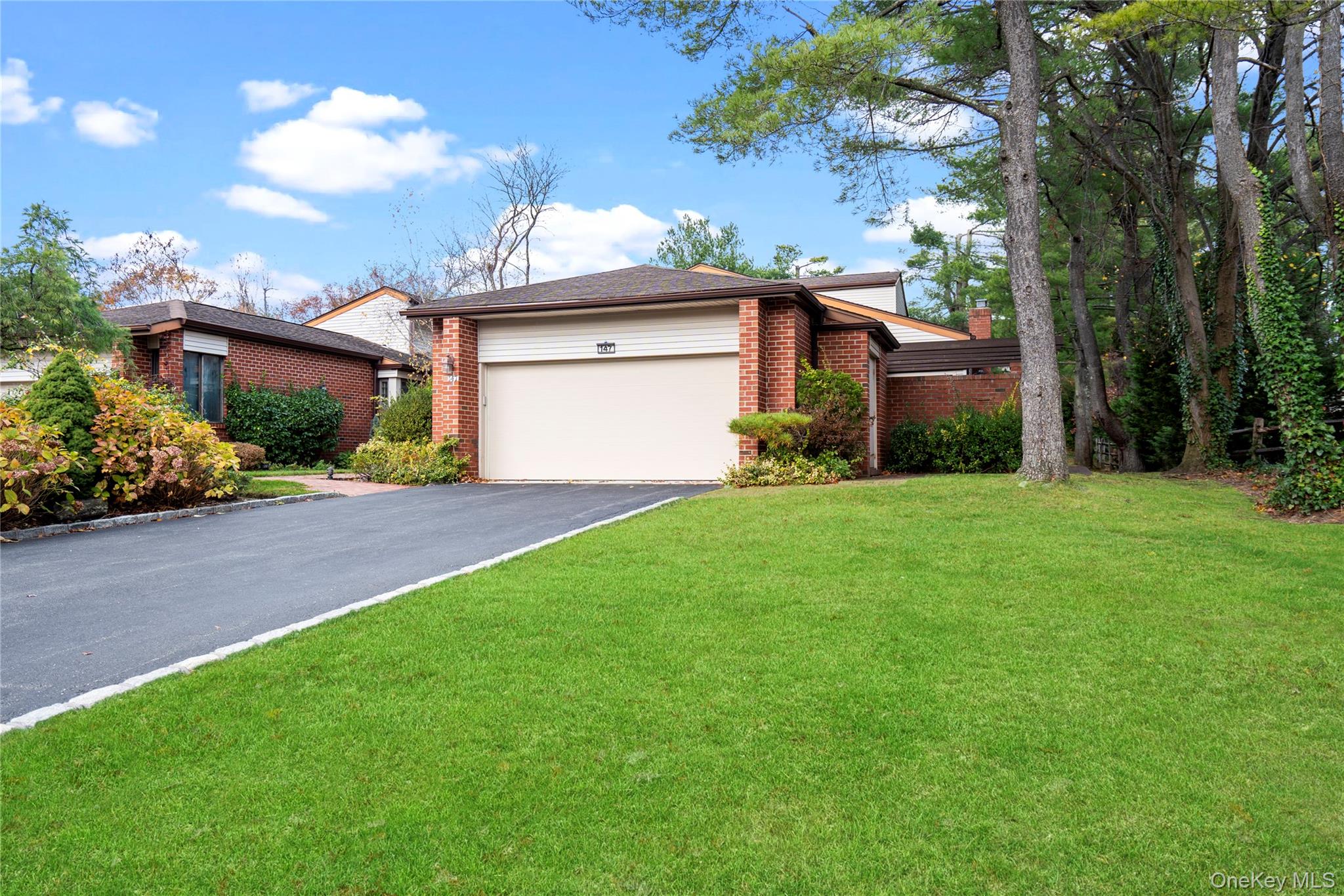View of front of house featuring brick siding, a front lawn, asphalt driveway, a garage, and a chimney