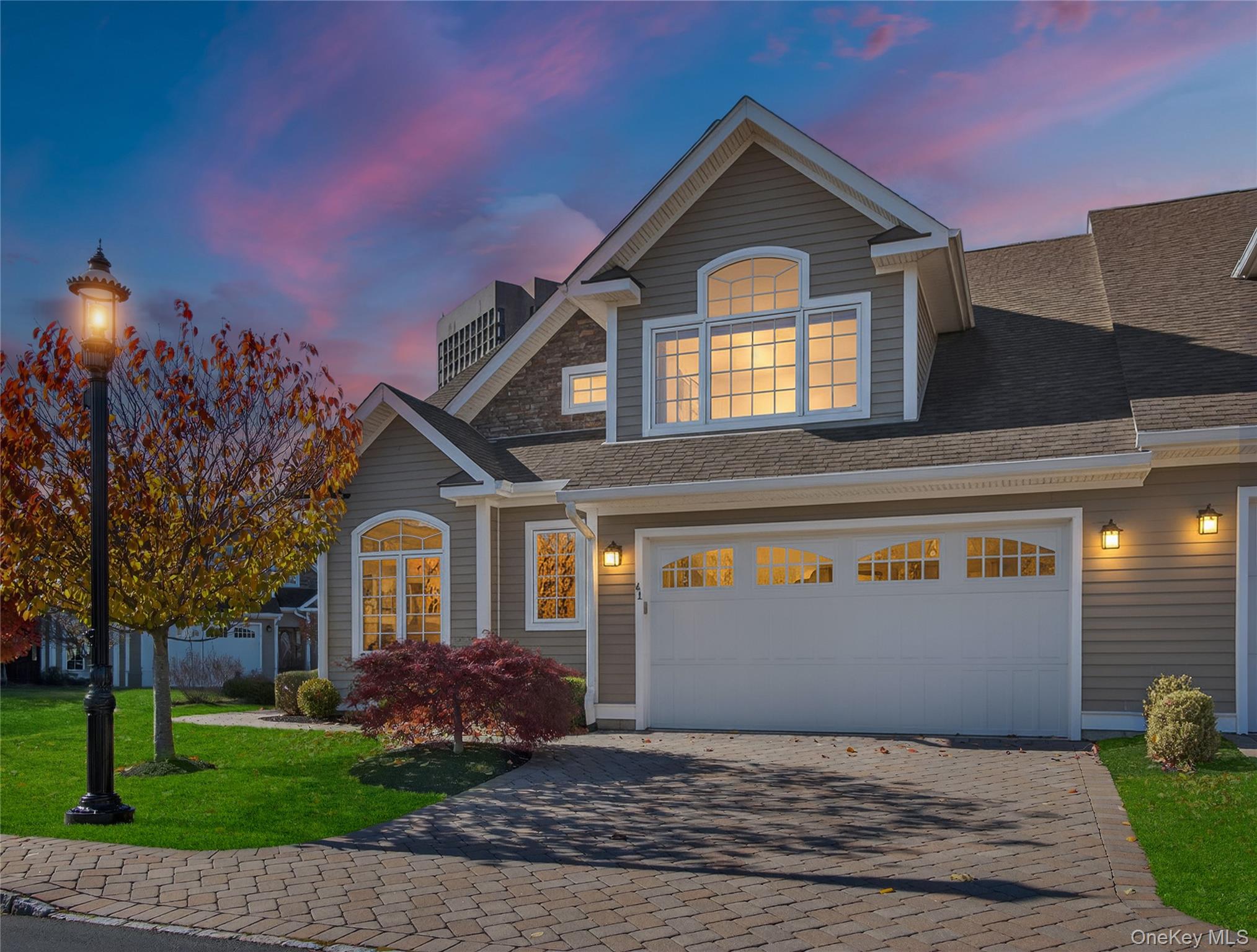 View of front of property with decorative driveway, a front lawn, a shingled roof, and a garage