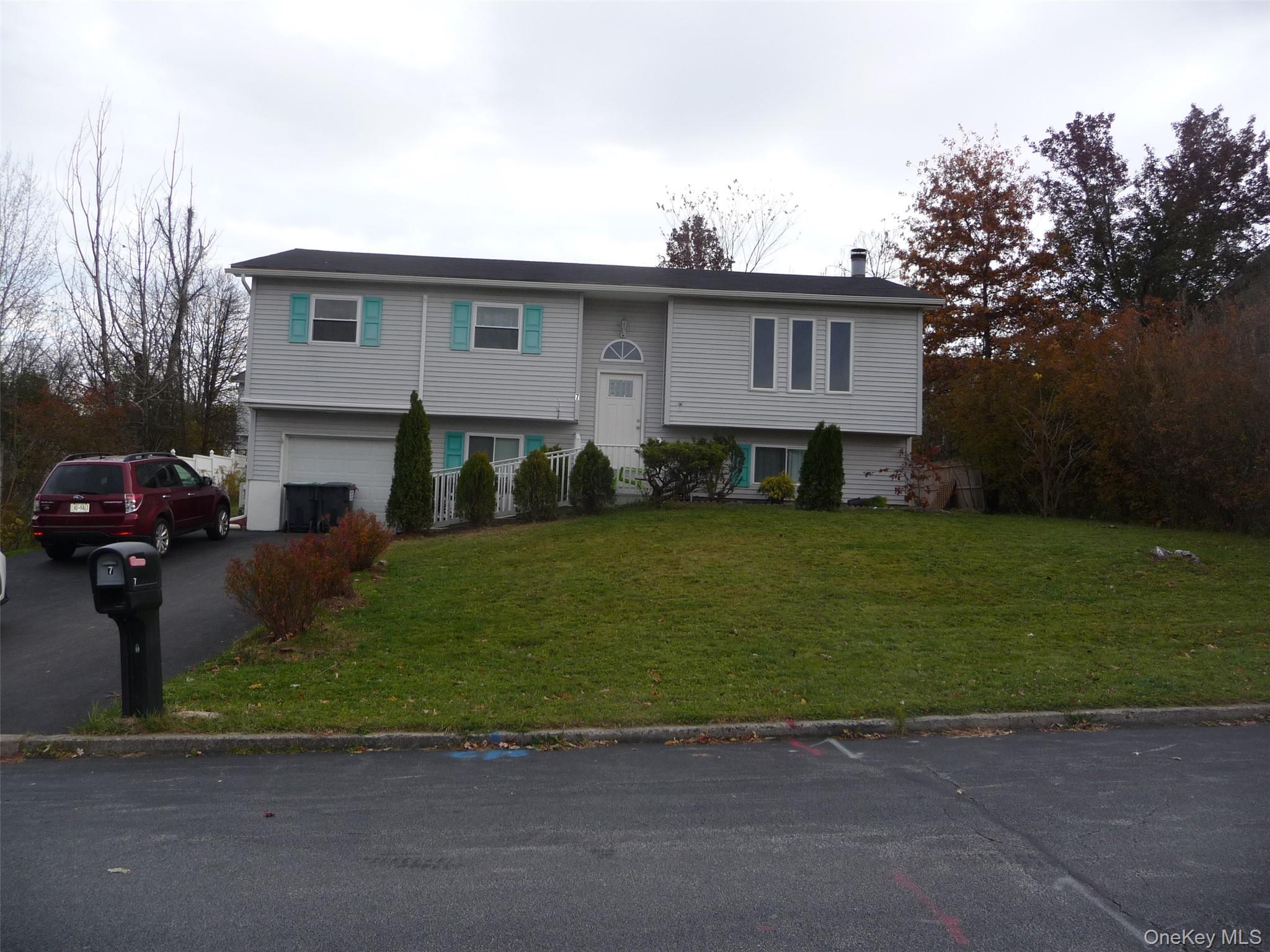 Bi-level home featuring driveway, a front yard, a chimney, and an attached garage