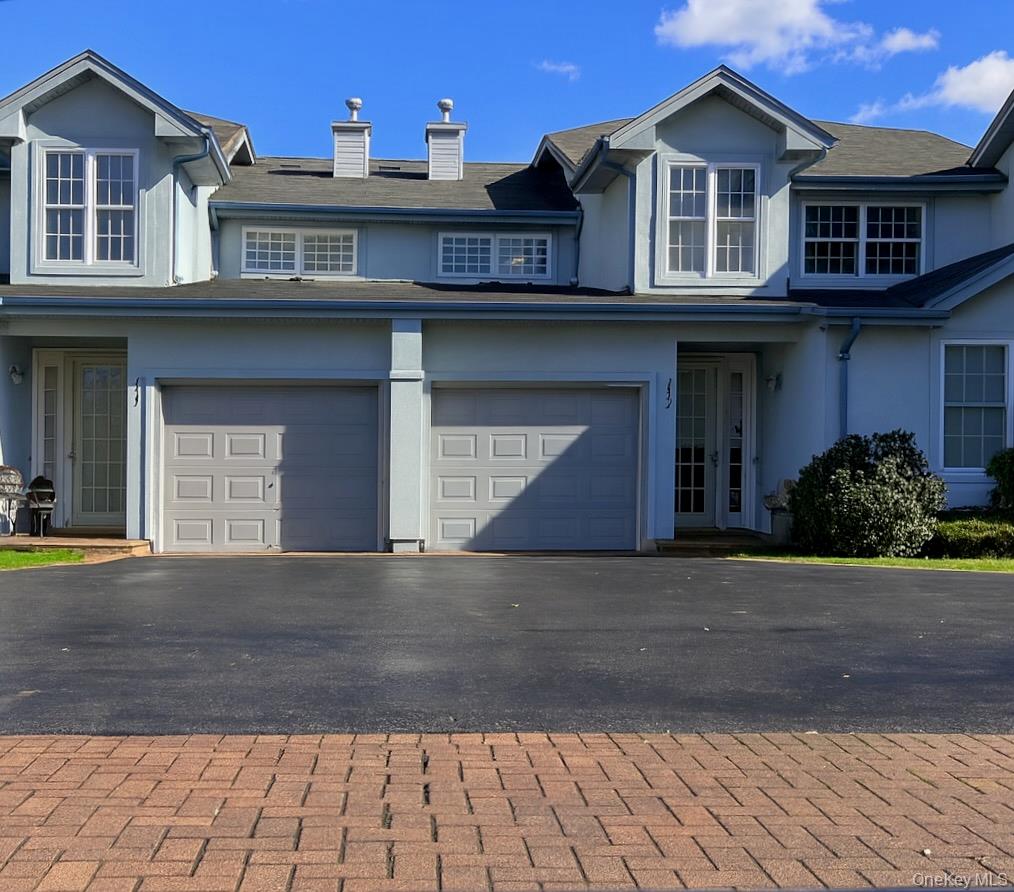 Traditional-style house featuring stucco siding, asphalt driveway, a chimney, and an attached garage